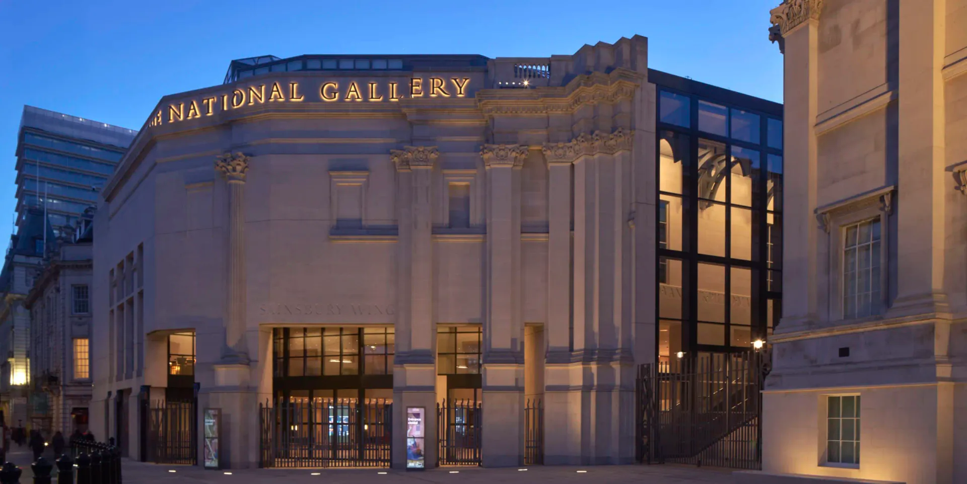 The National Gallery's neoclassical facade illuminated at dusk, featuring restored stone columns and a modern glass extension, designed by Annabelle Selldorf.