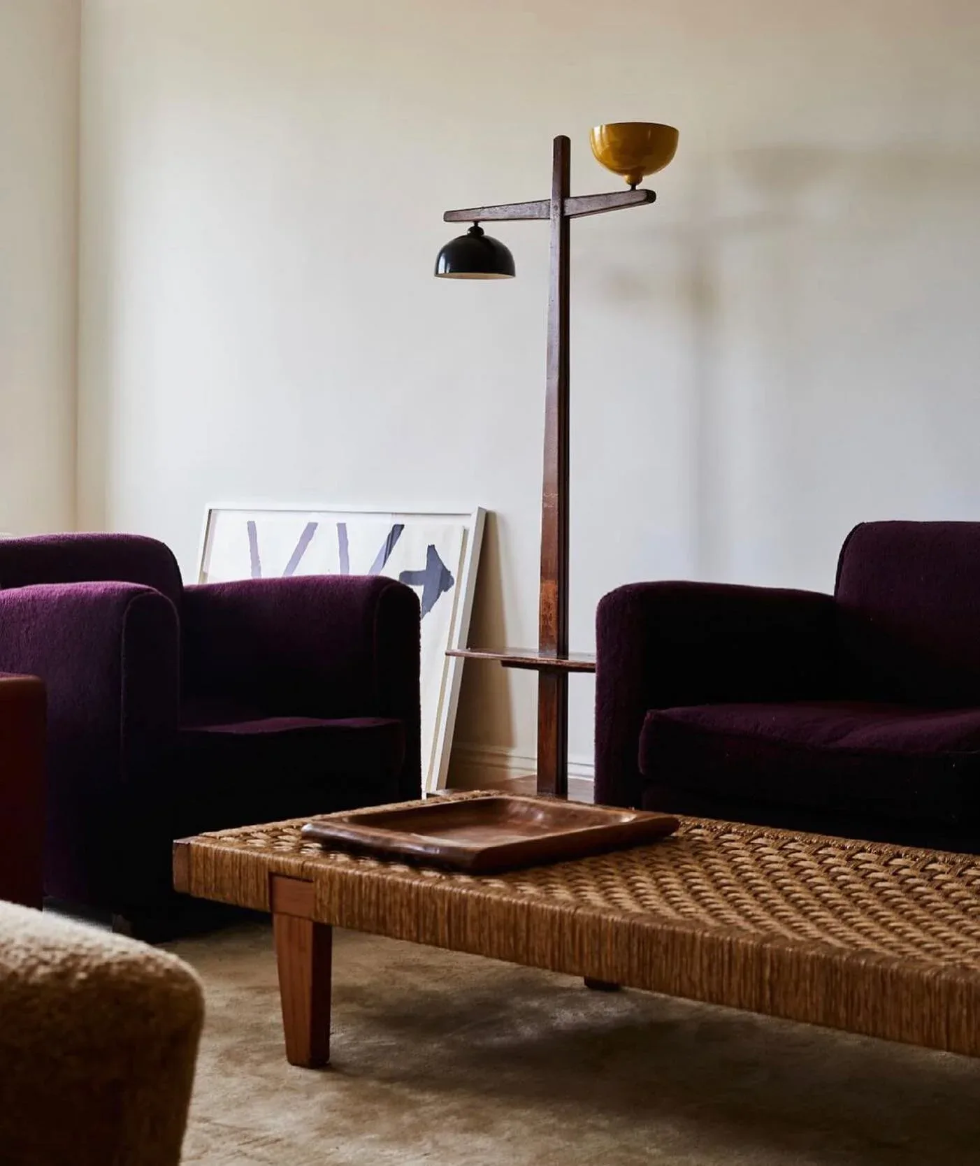 Modern living room with deep purple velvet armchairs, woven wood coffee table, brass floor lamp, and neutral tones by Annie Nelson.