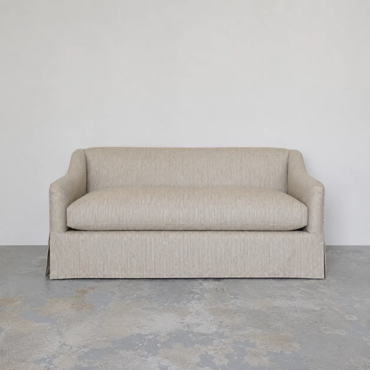 Beige upholstered sofa with vertical ribbed fabric and skirted base in a minimalist interior space by Antony Todd.