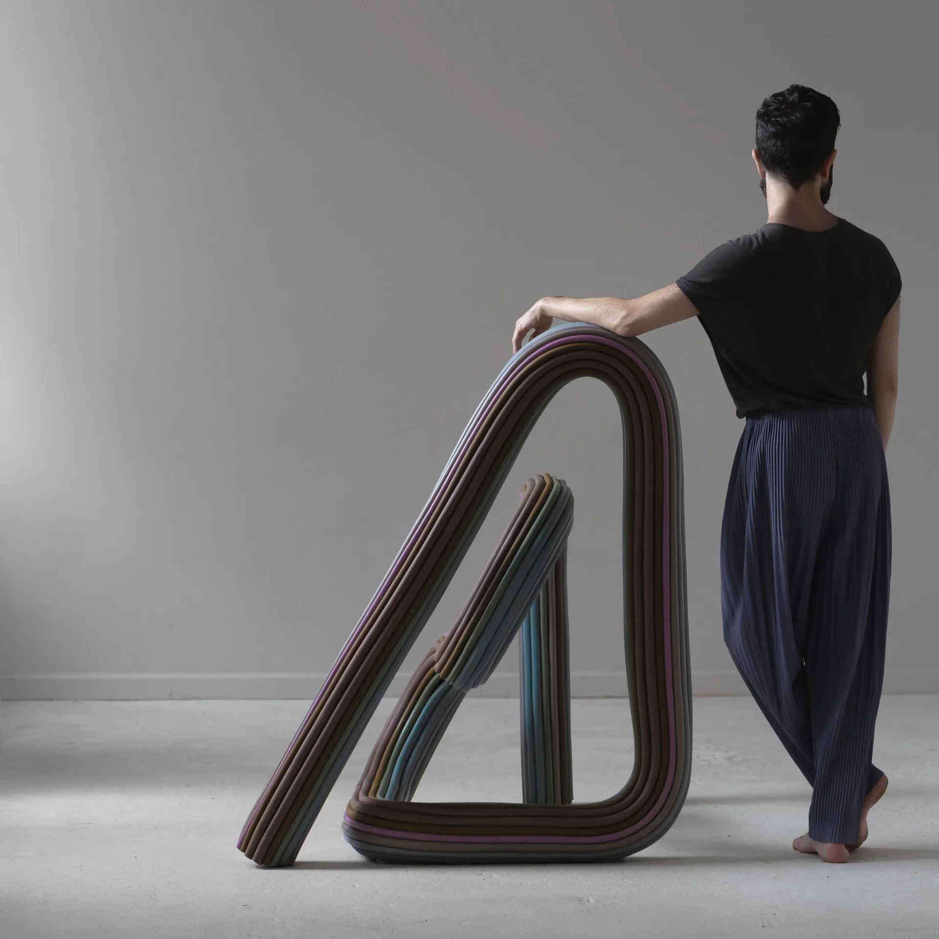 Woman posing beside an undulating sculptural installation with curved striped forms in brown and gray tones by Ara Thorose.