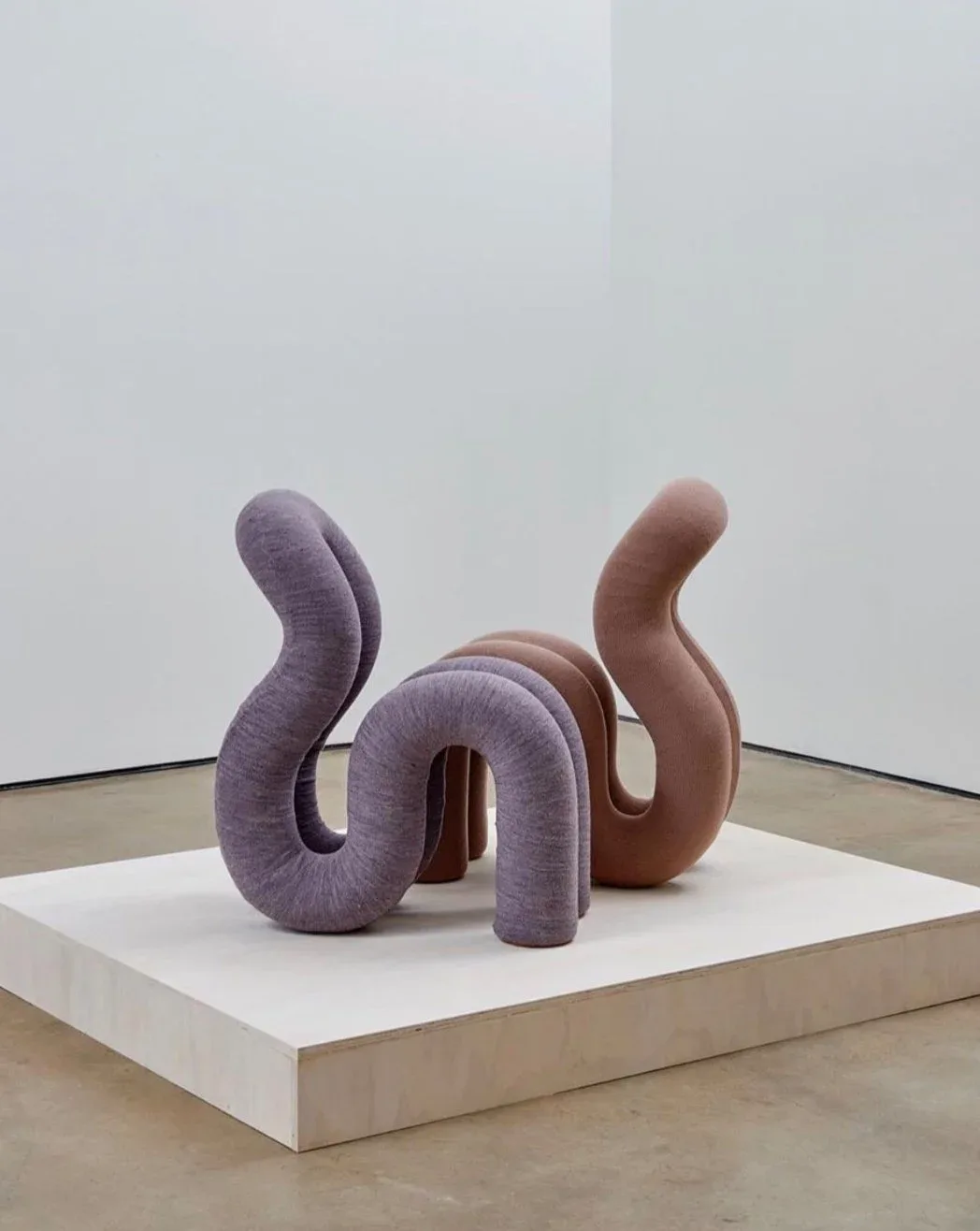Abstract sculptural installation featuring curved fabric-wrapped forms in purple and terracotta tones on a white platform by Ara Thorose.