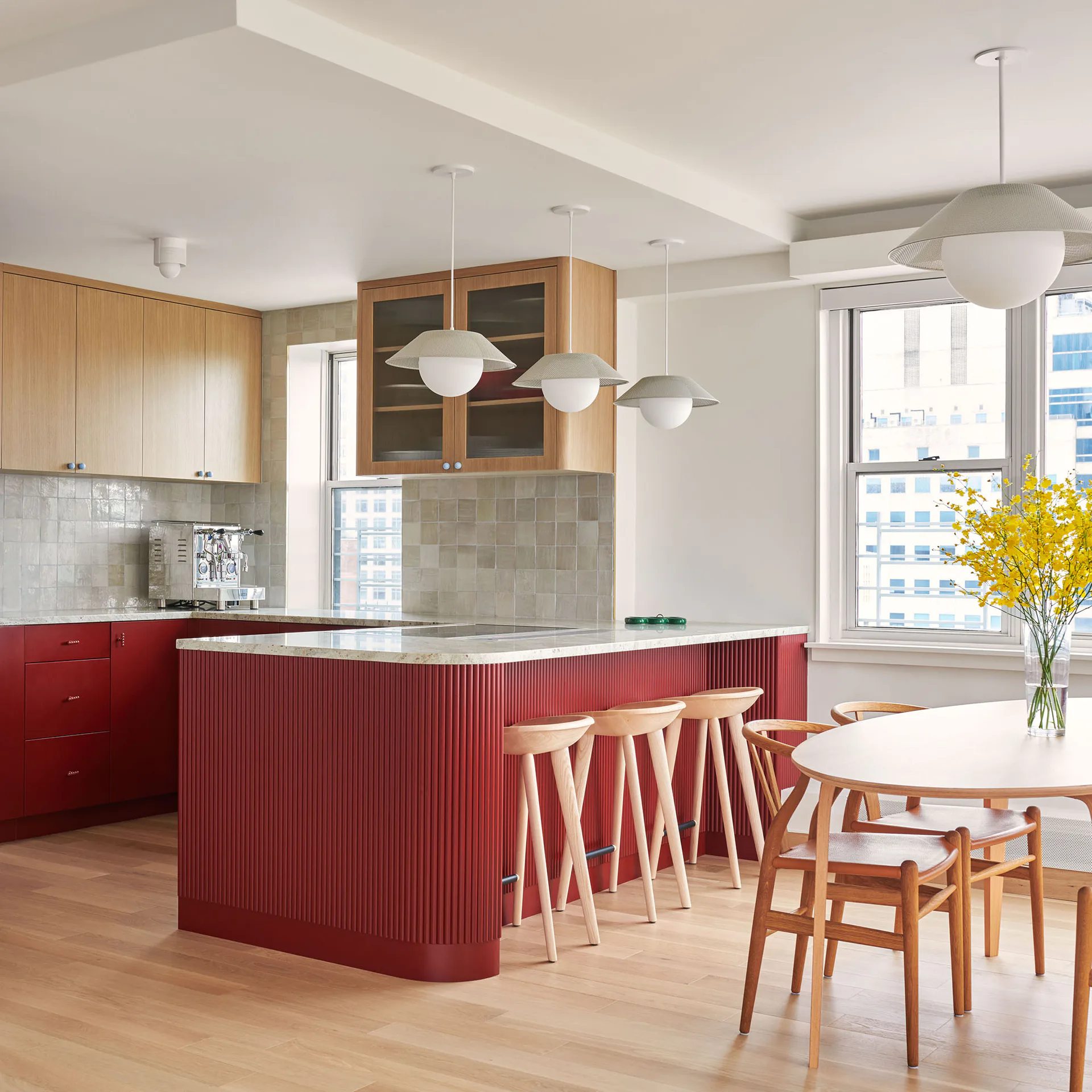 Modern kitchen with red ribbed cabinetry, natural wood accents, white countertops, pendant lighting, and dining area with wooden chairs by Aria Jahanshahi.