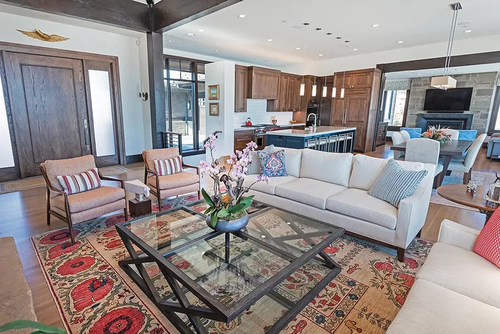 Open-plan living room with light gray sofa, striped accent chairs, geometric glass coffee table, and colorful patterned rug by Arlene Reilly.