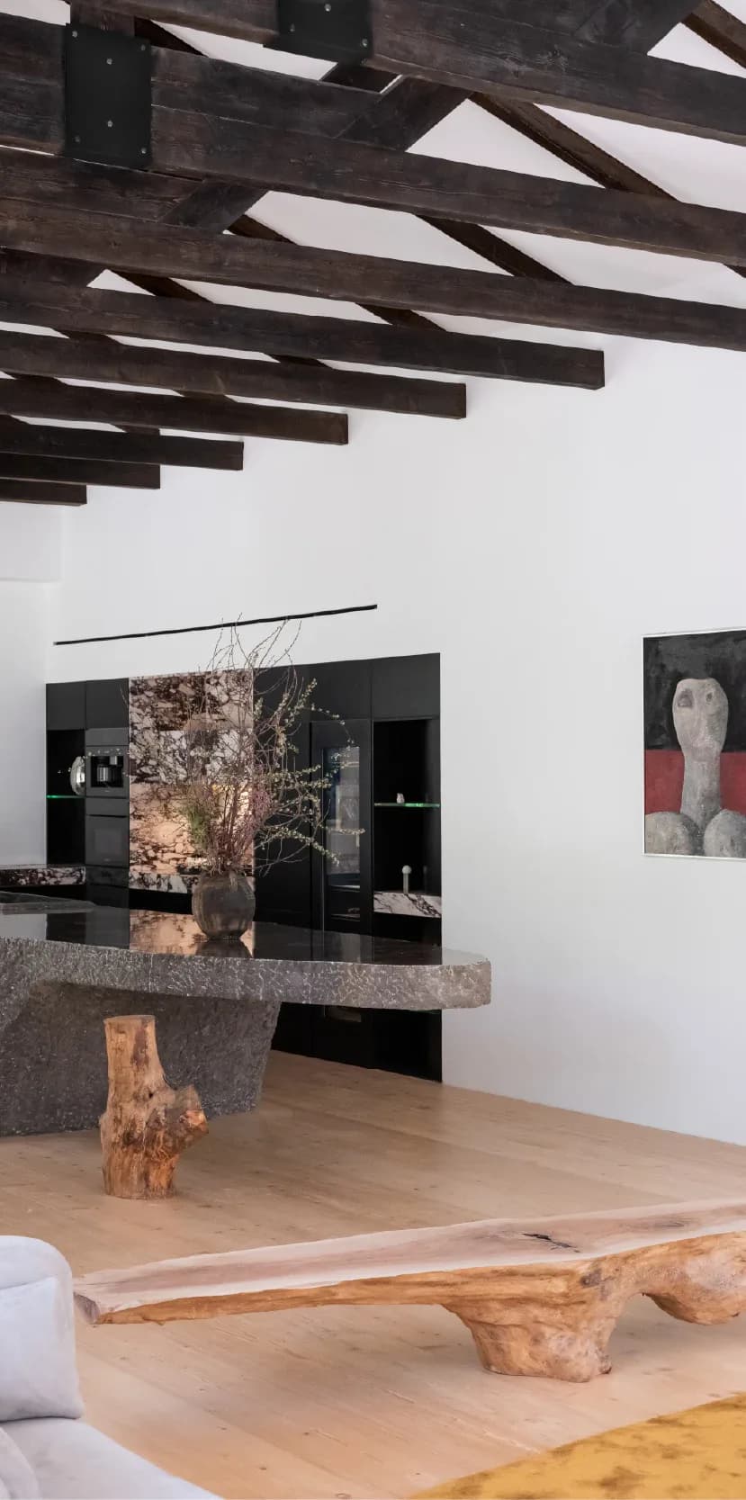 Modern interior with exposed dark wooden ceiling beams, white walls, black cabinetry, natural wood furniture pieces, and artwork—a contemporary residential design by Arman Safavi.