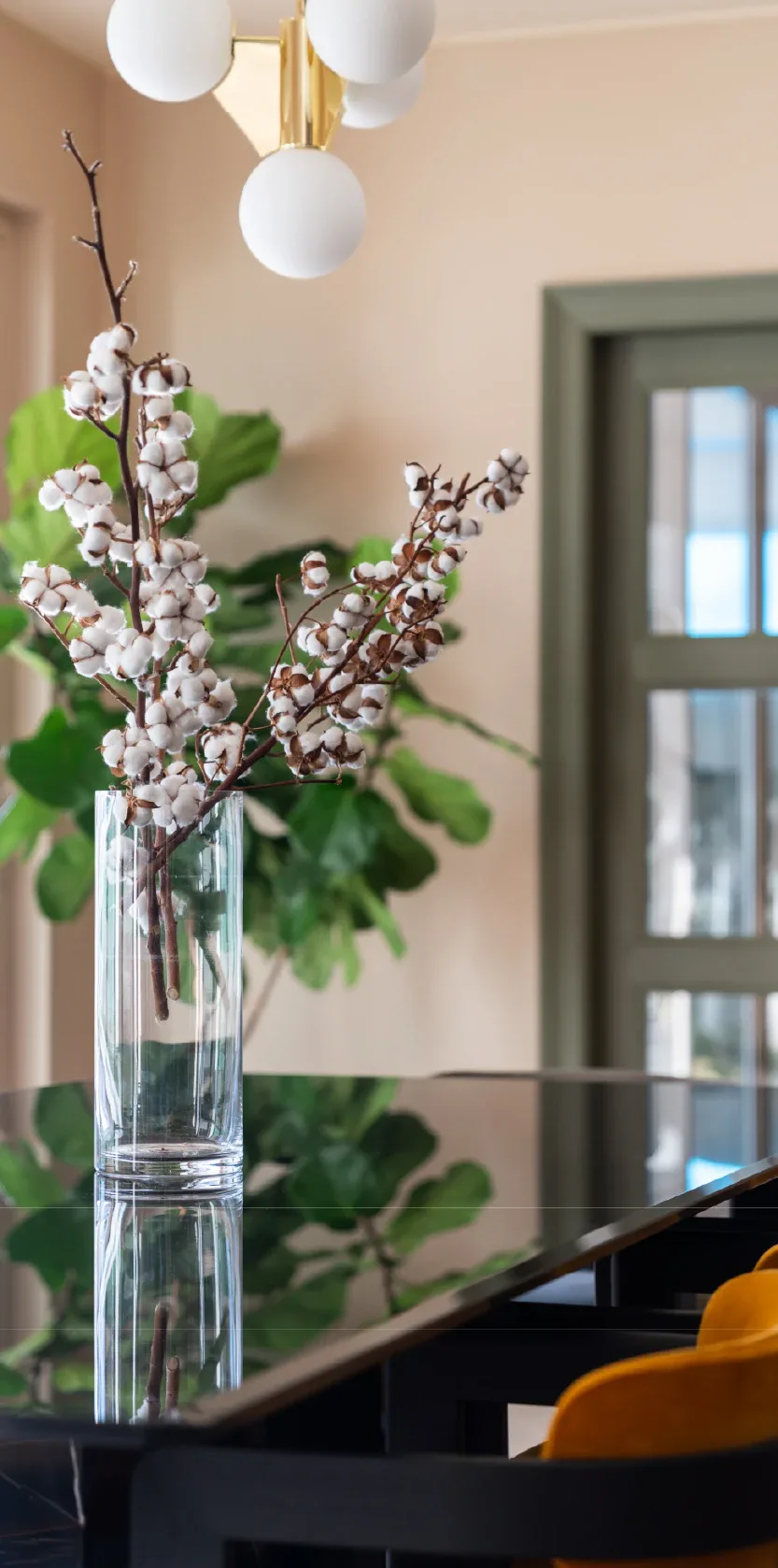 Modern entryway with cream walls, brass globe pendant light, and clear glass vase with white flowering branches and greenery by Arman Safavi.