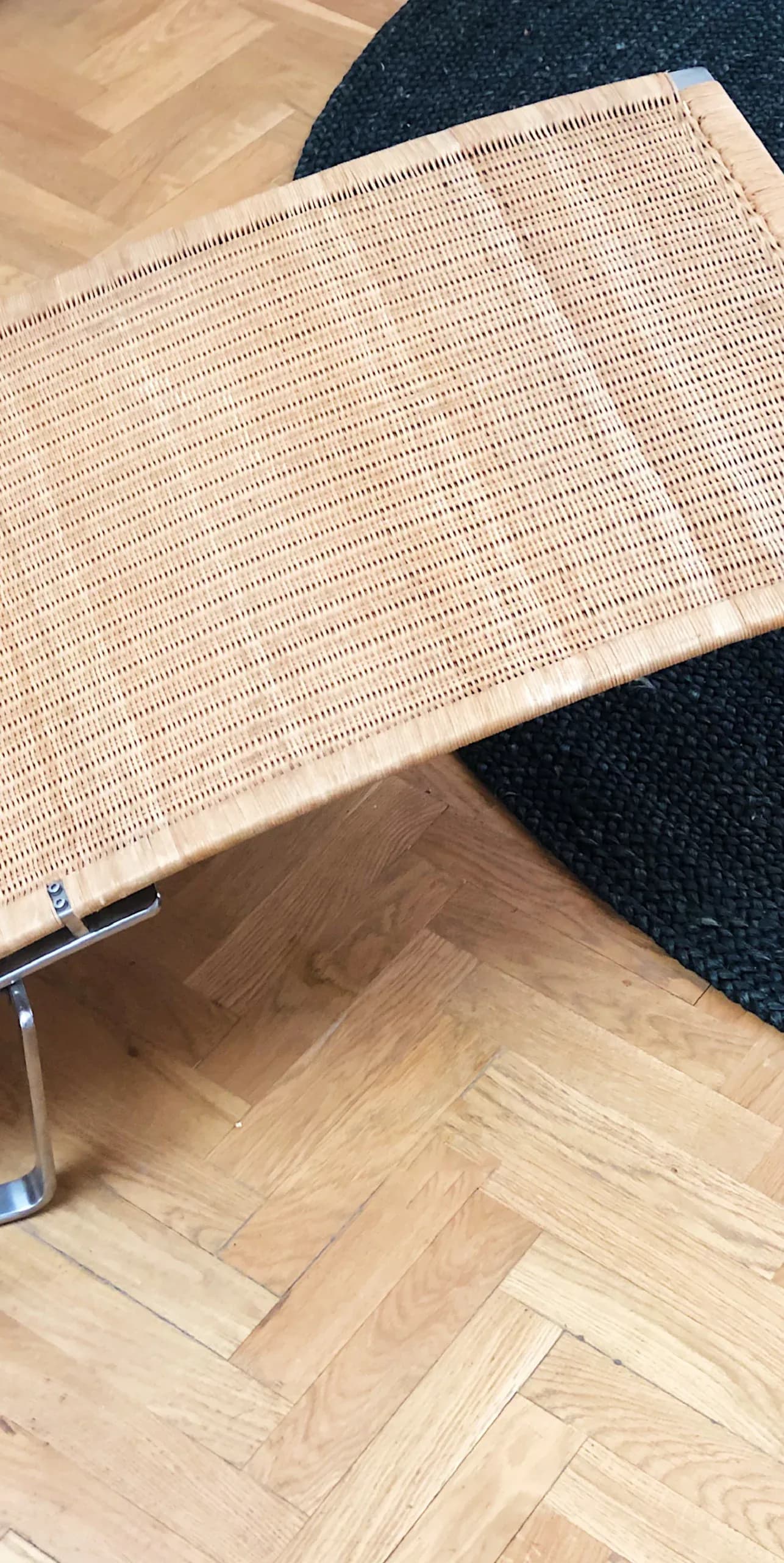 Modern seating with woven rattan backrest and metal frame on dark carpet, alongside light wood herringbone flooring by Arman Safavi.