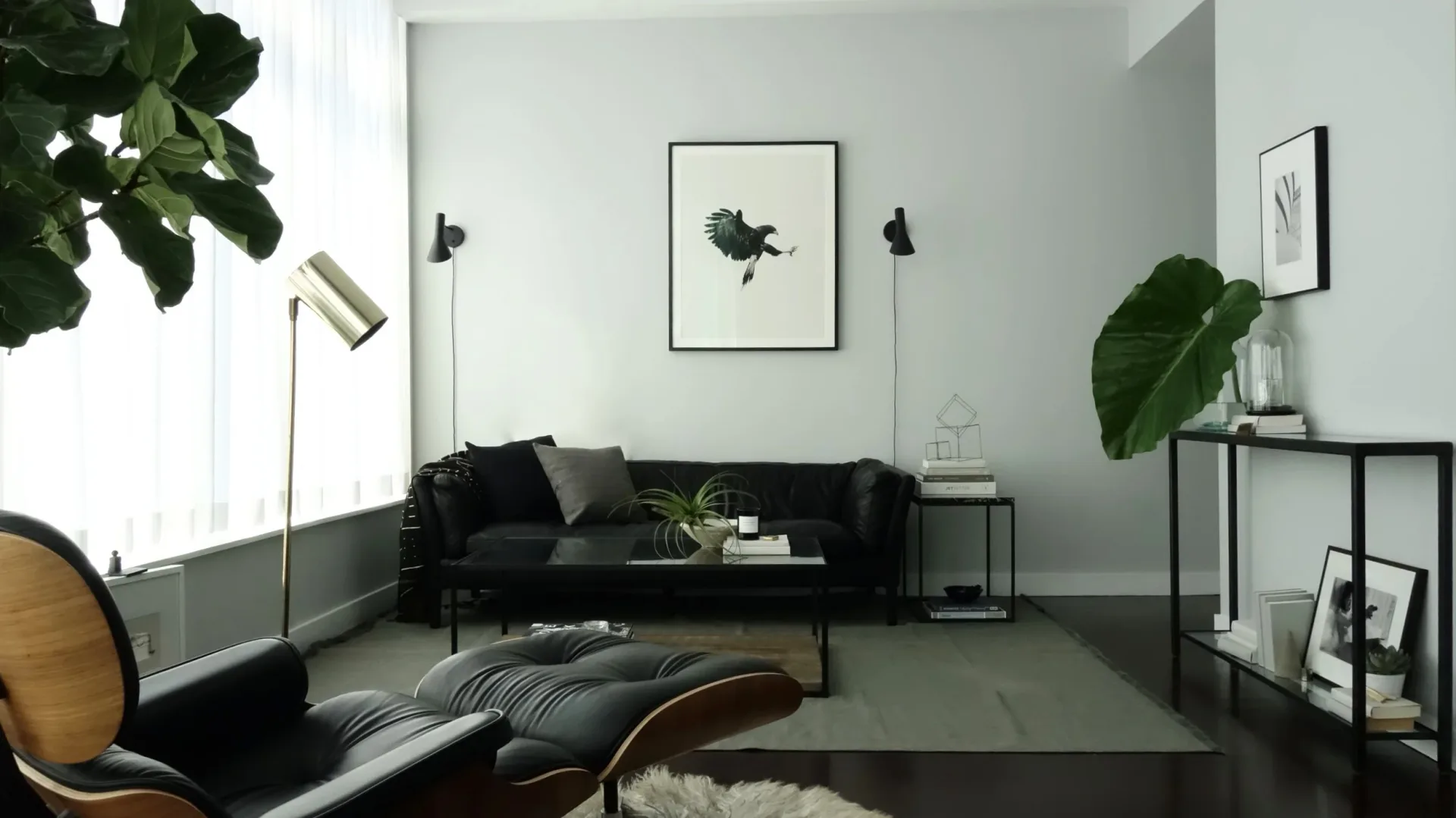 Modern living room with black sofa, dark flooring, and minimalist décor featuring plants and artwork by Armann Ortega.