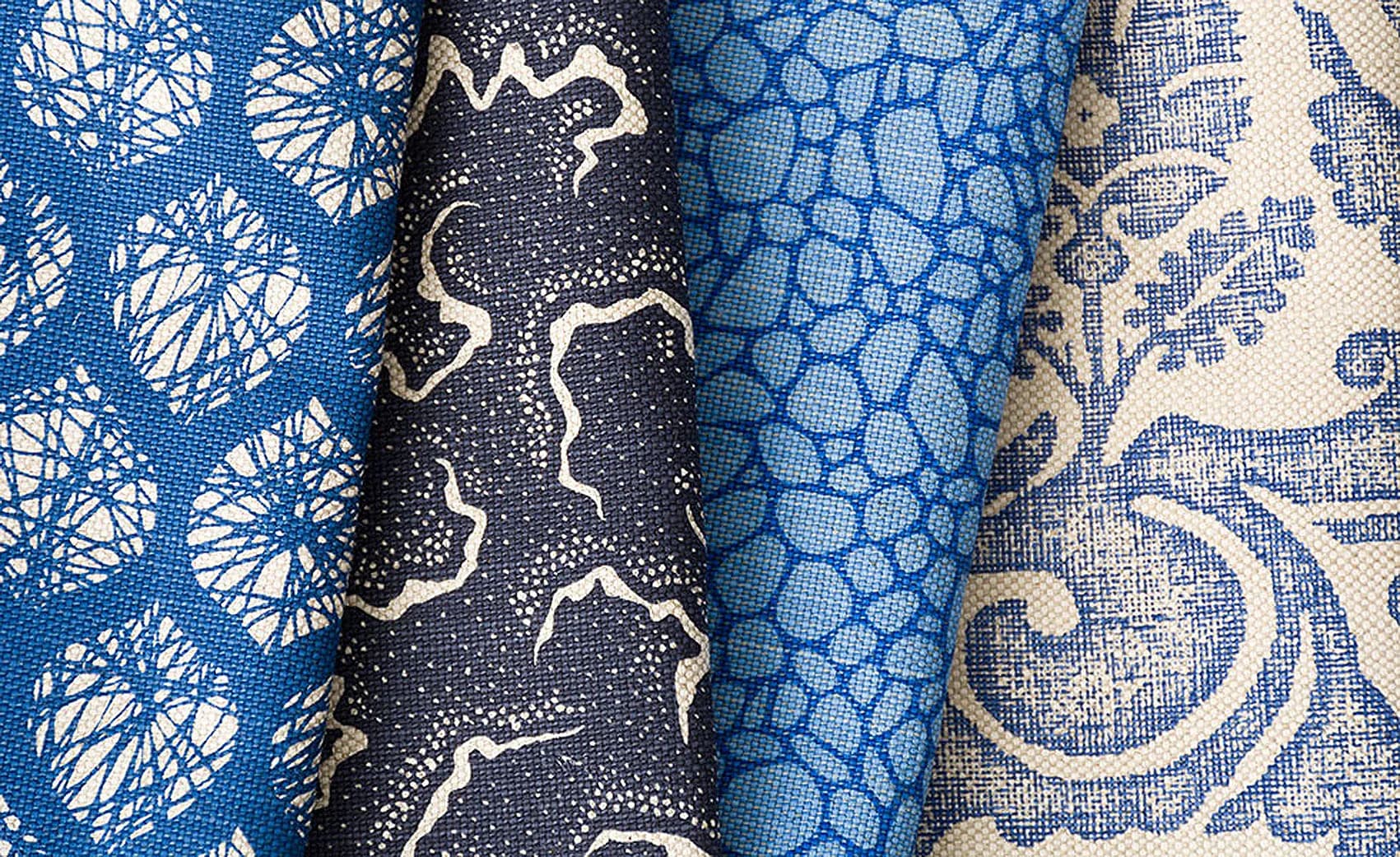 Five rolled fabric samples in blue and navy tones displaying varied patterns including geometric, floral, and textural designs by Ashley Hicks.