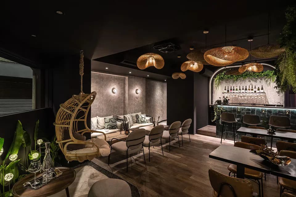 Modern lounge interior with woven pendant lights, rattan swing chair, dark wood flooring, and lush greenery, designed by Ashley Liu.