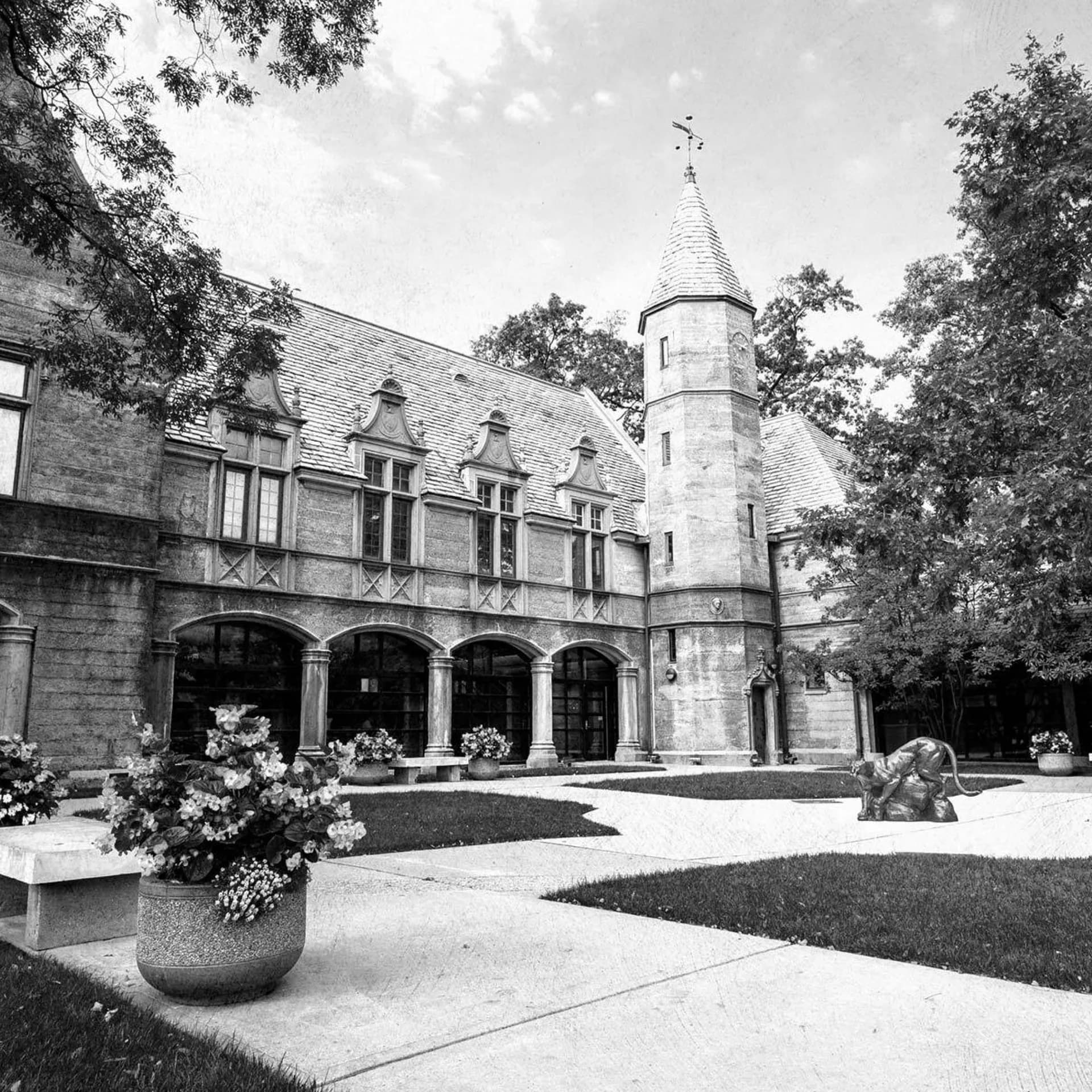 Stone courtyard with arched colonnade, round turret, manicured lawn, and planted urns, architectural design by Ashley Massano.