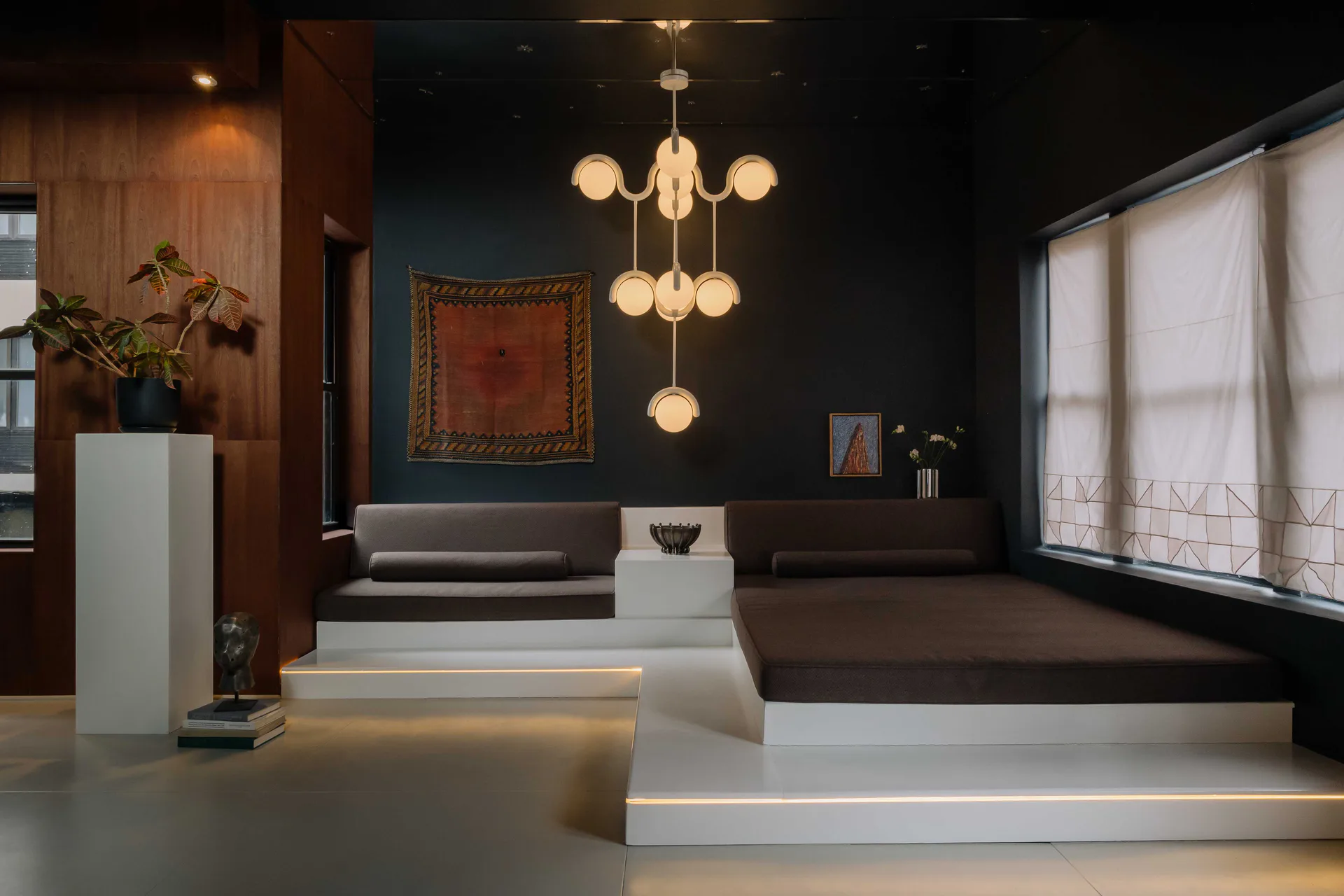 Modern lobby interior with white stepped reception desk, dark accent wall, brass pendant lighting, wooden paneling, and minimalist furnishings designed by Astraeus Clarke.