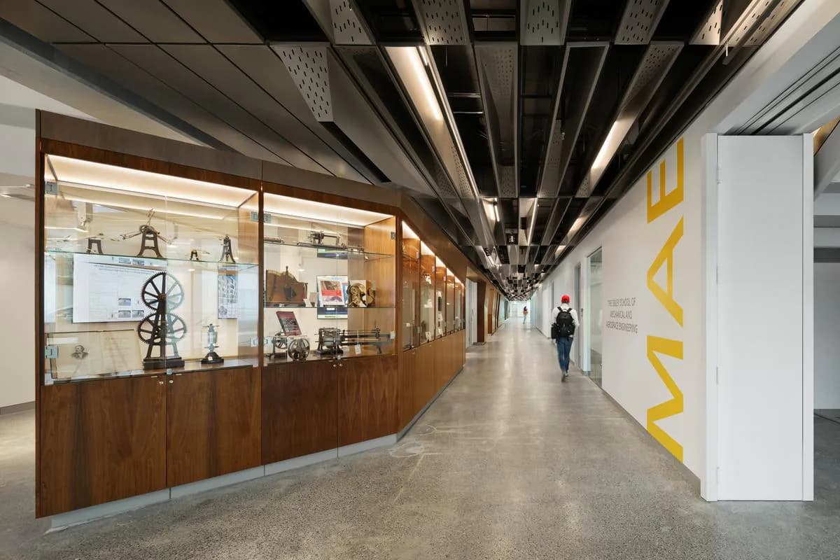 Modern corridor with wood-paneled display cases, linear ceiling details, polished concrete flooring, and yellow accent signage, designed by Attila Uysal.