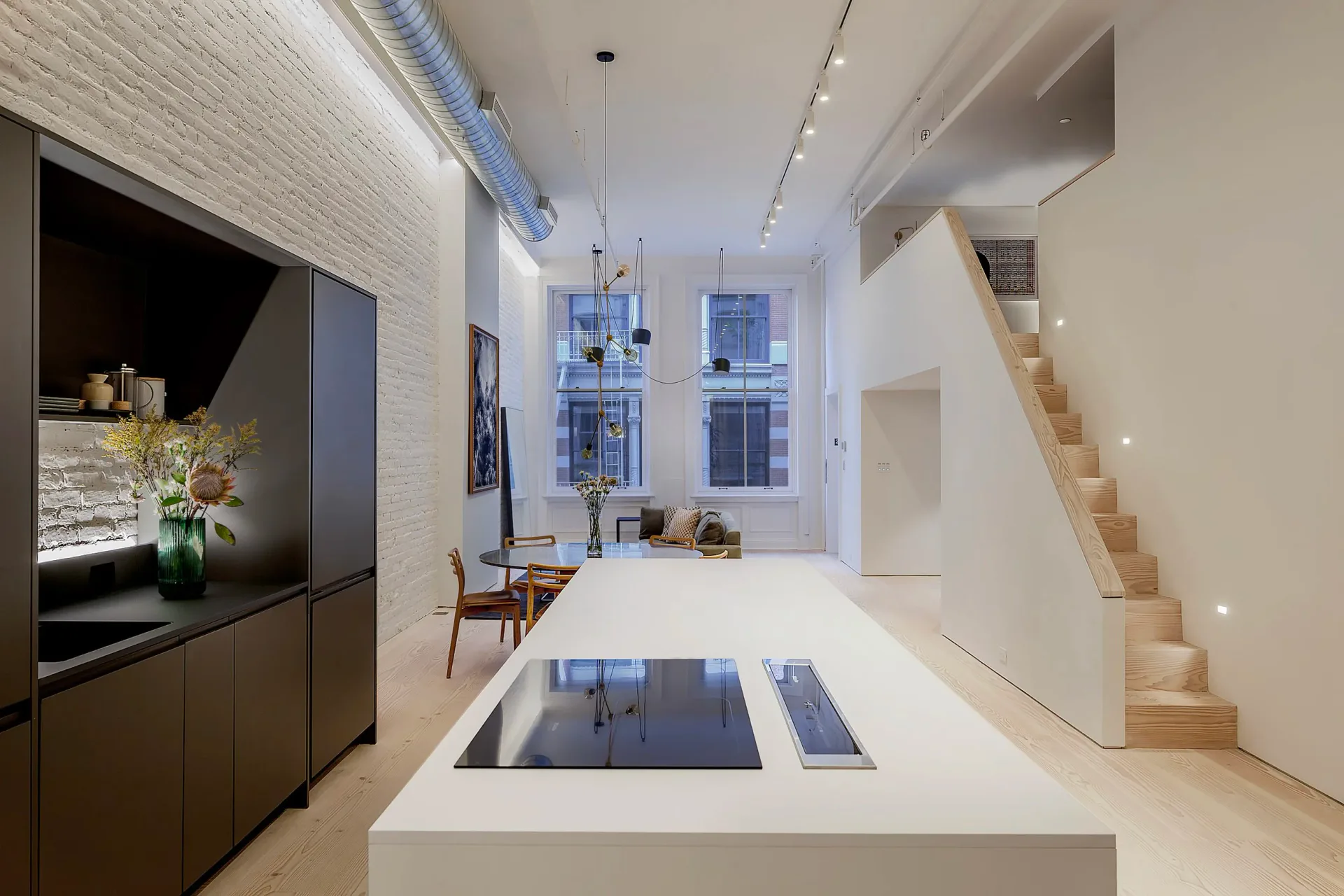 Modern loft interior with white flooring, minimalist kitchen, central island, wooden staircase, and floor-to-ceiling windows by August Liau.