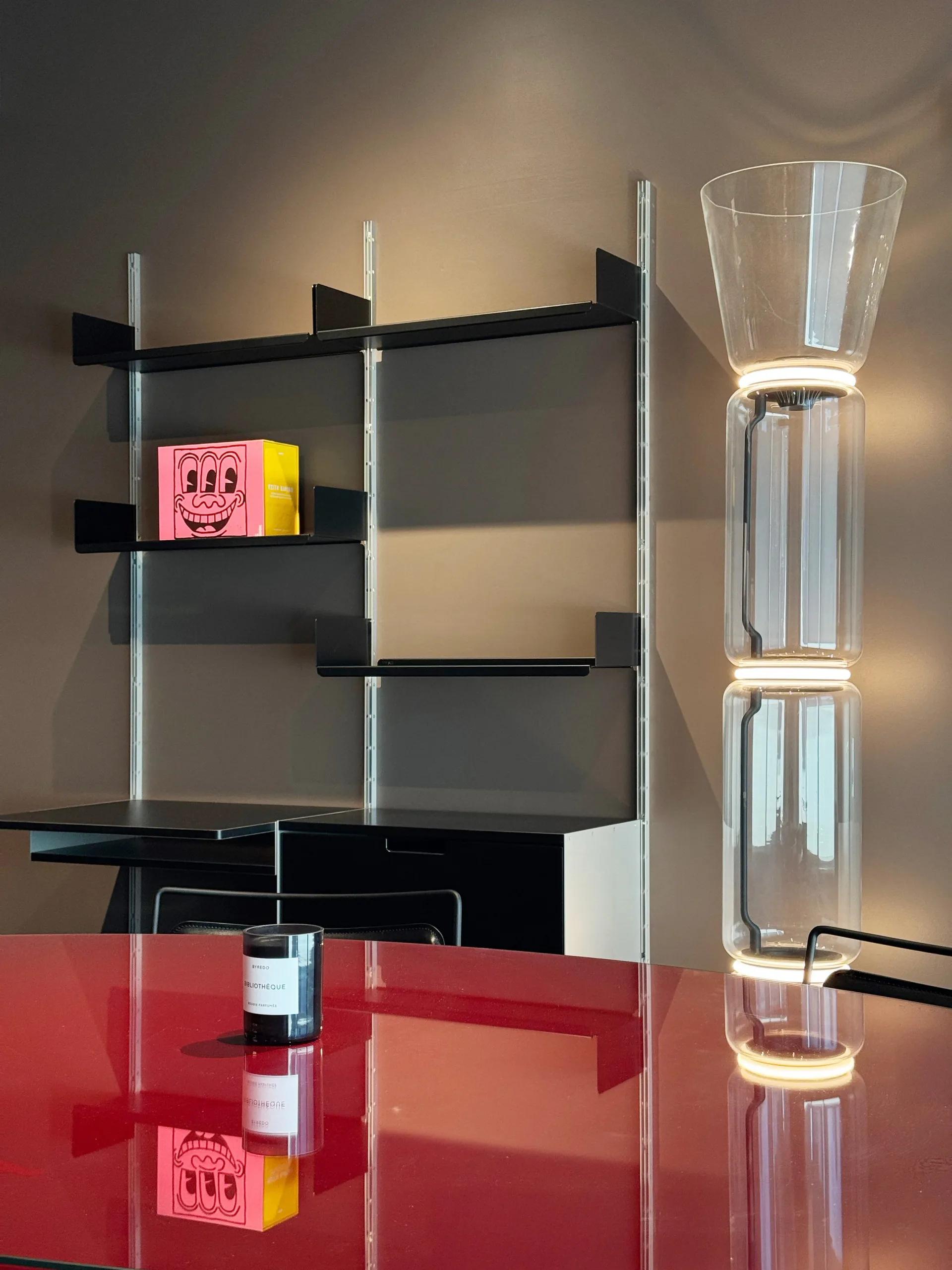 Contemporary interior installation featuring modular black shelving with glass supports, red base platform, stacked glass vessels, and pink sculptural objects, designed by August Liau.