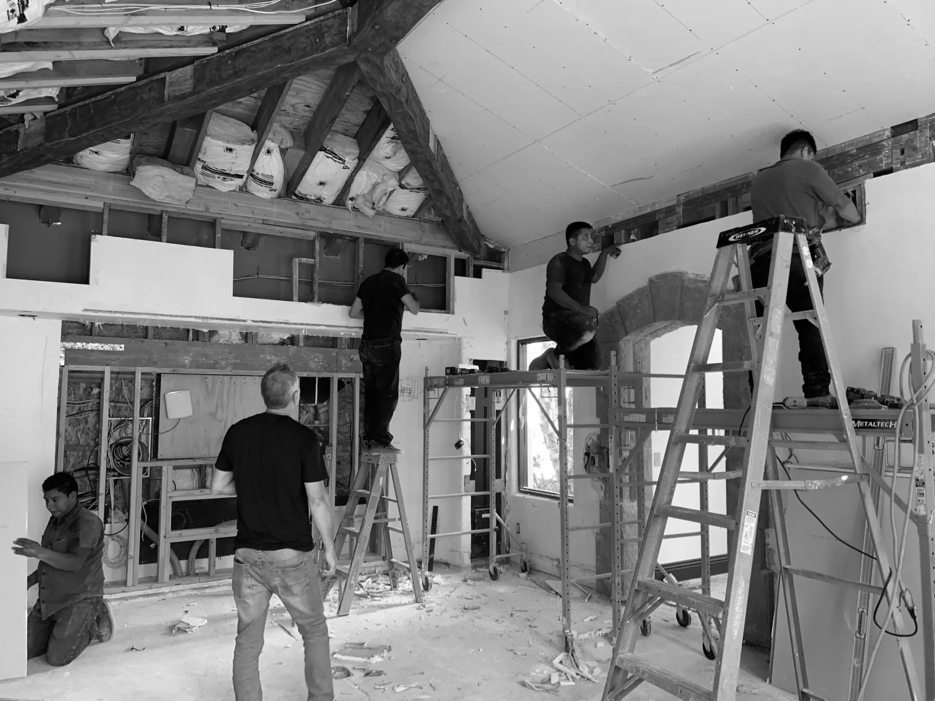 Interior renovation in progress showing exposed ceiling beams, white drywall, and construction scaffolding during active build-out by Ava Lunder.
