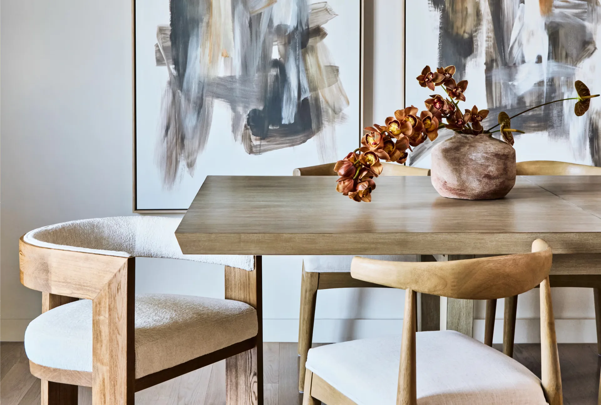 Mid-century modern dining room with natural wood table, upholstered chairs, abstract artwork, and dried botanical arrangement by Avery Johnson.