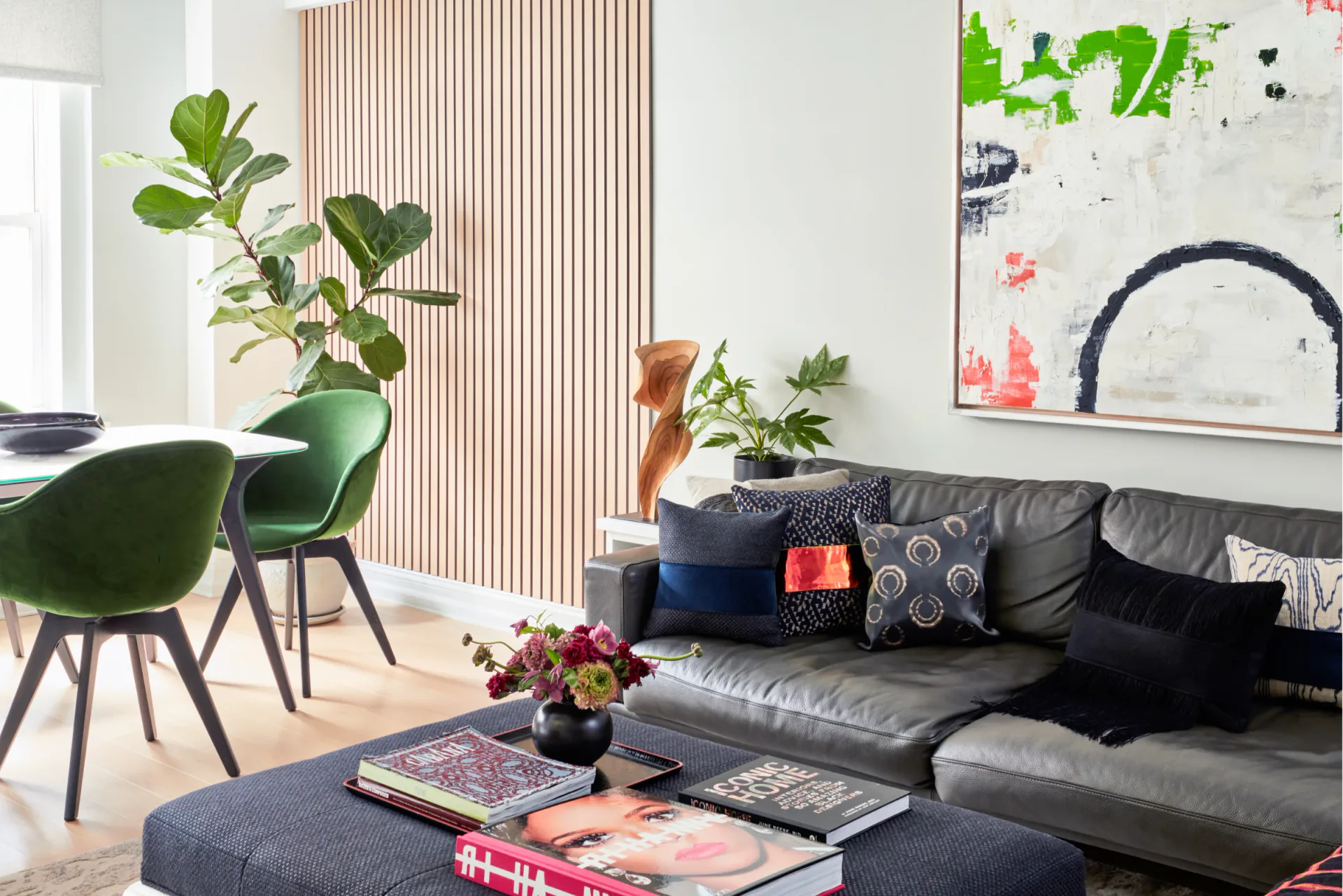 Modern living room with black leather sofa, green accent chair, blue round ottoman, potted plants, and abstract artwork, designed by Avery Johnson.