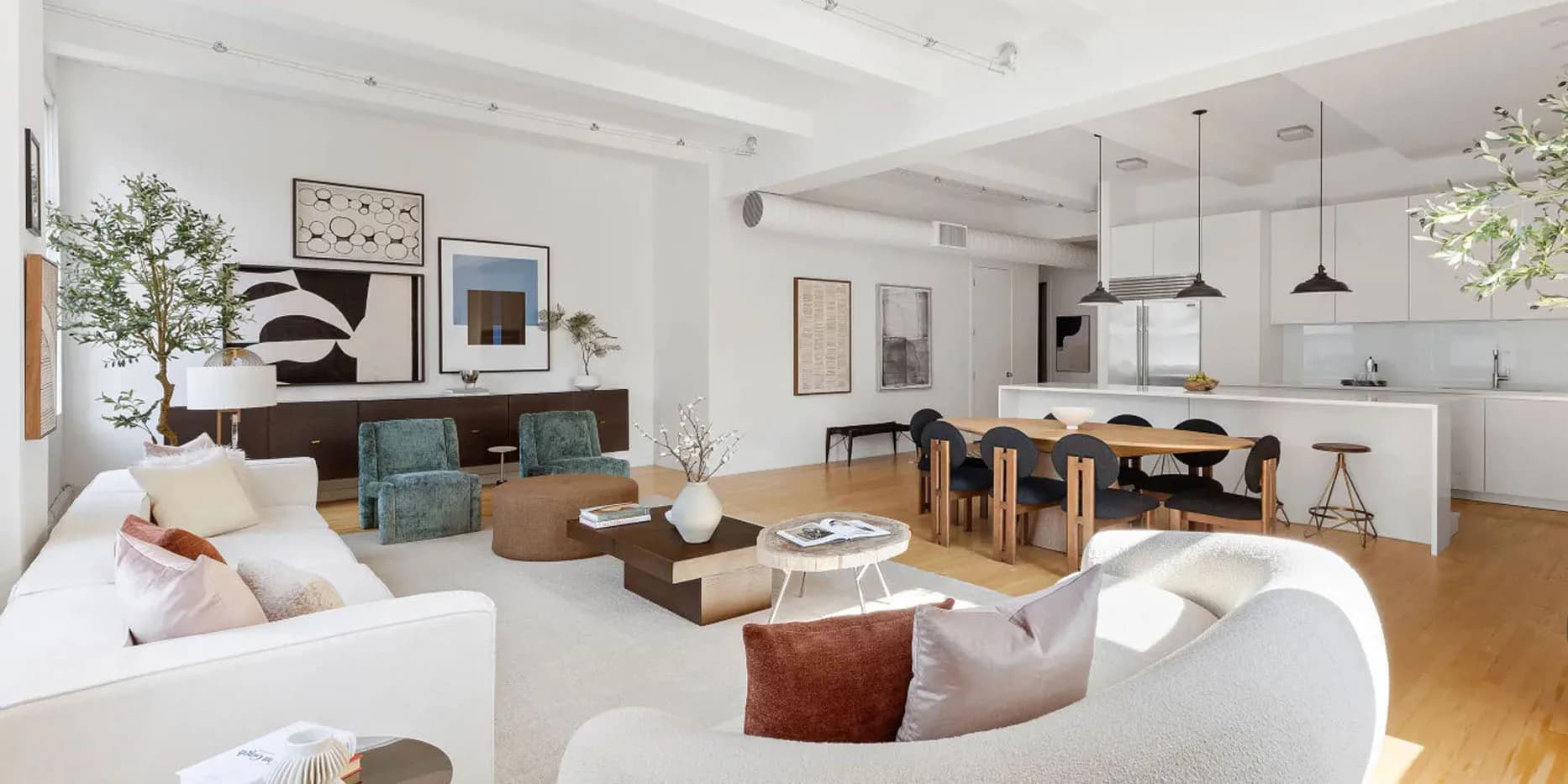 Open-plan residential interior with curved white furniture, wooden dining table, glass kitchen partition, and warm natural lighting by Ayhan Ozan.