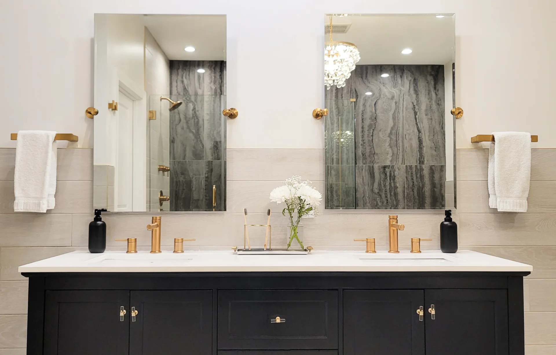 Modern bathroom with black dual vanity, white subway tile walls, dual mirrors with brass fixtures, and dark marble shower surround by Bailee Klein.