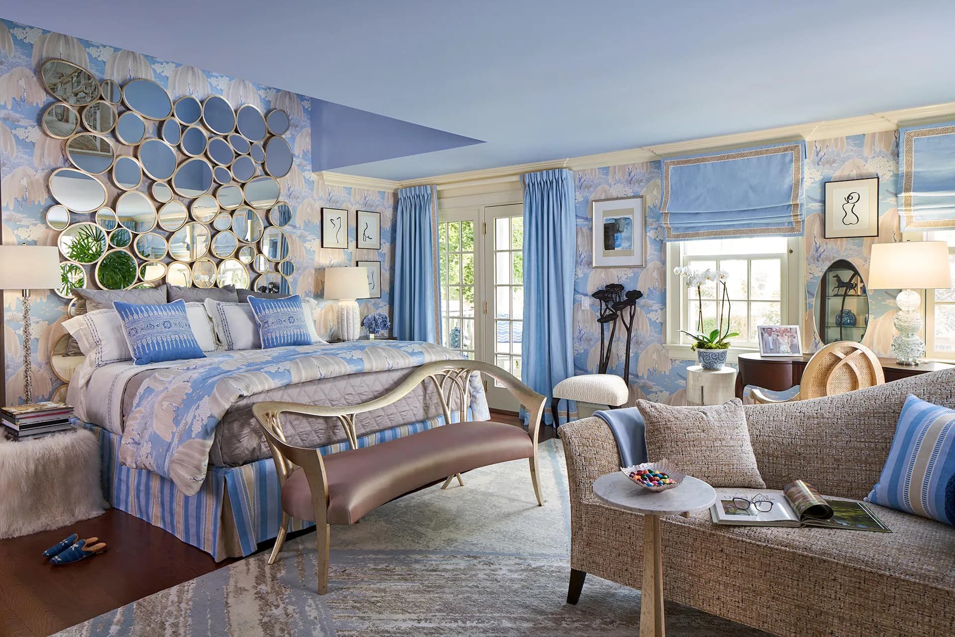 A sophisticated blue and white bedroom suite features a decorative plate wall installation, striped upholstered seating, and coordinated drapery, designed by Barbara Ostrom.