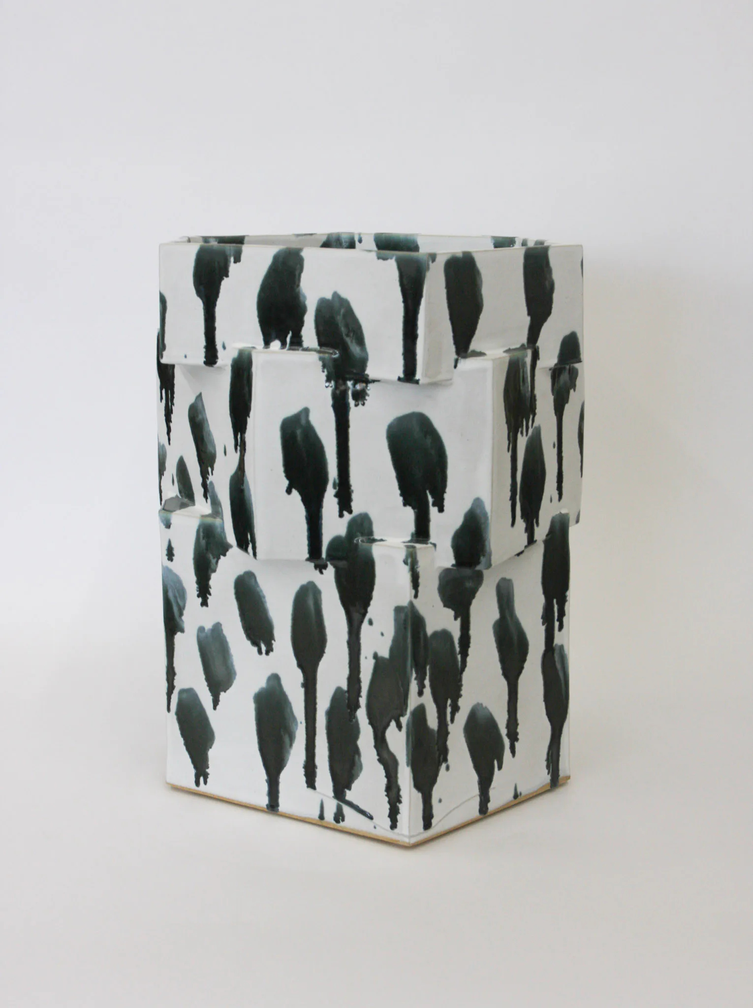 White cylindrical ceramic vessel with dark green tree silhouettes printed across all sides, displayed against a neutral background by Bari Ziperstein.