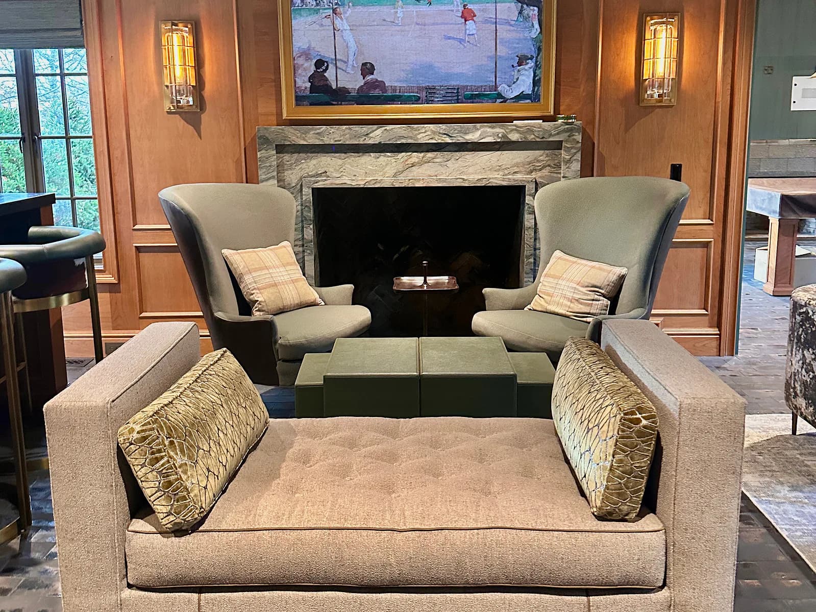 Luxury living room featuring a cream upholstered sectional with gold accent pillows facing a stone fireplace, flanked by two modern armchairs and sconces, designed by Batya Klein.