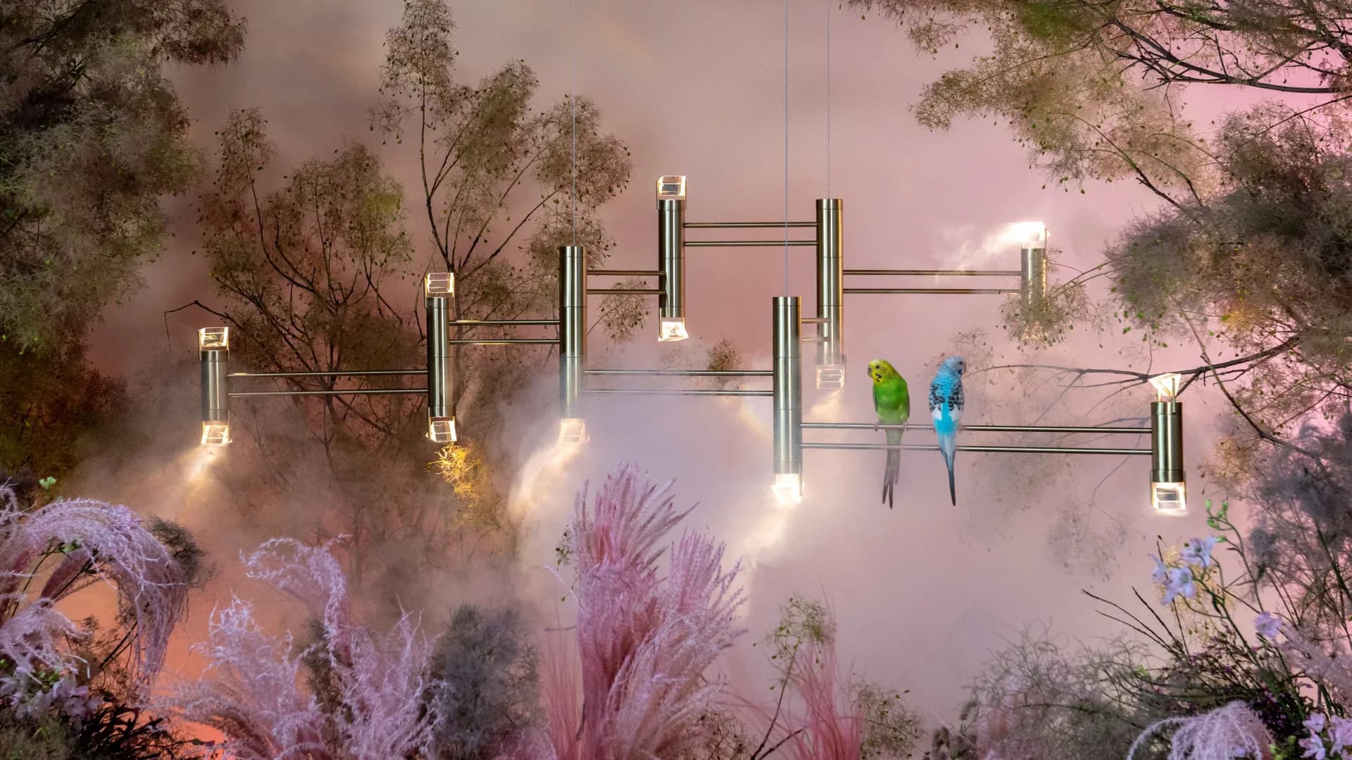 Ethereal forest landscape with suspended brass and steel lighting fixtures among misty pink-toned trees and purple flowering plants by Bec Brittain.