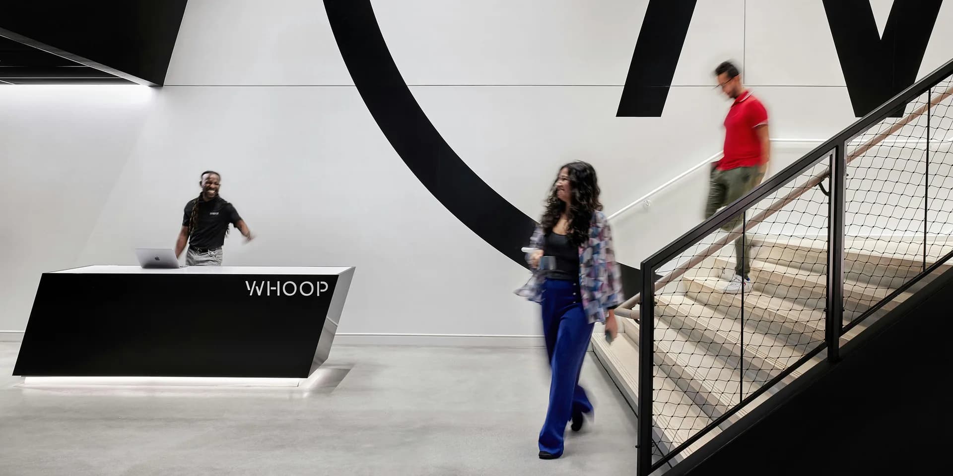 Modern interior space with large black sculptural letters, white walls, metal railings, and visitors on stairs by Belen Cavdar.
