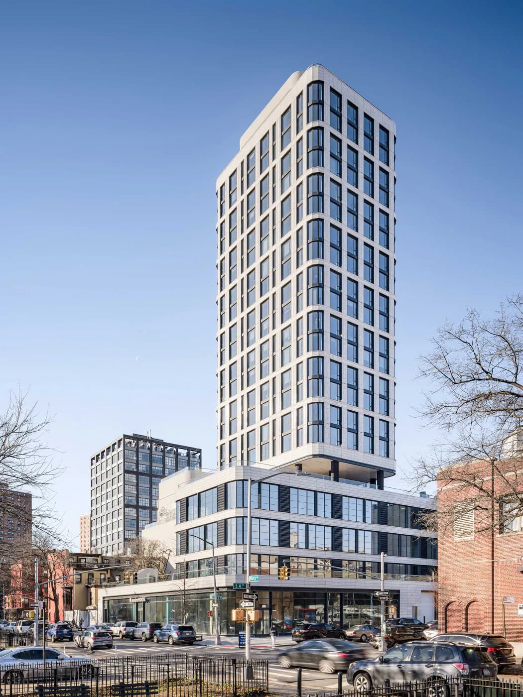Contemporary mixed-use building with cream and blue facade, curved base featuring ground-floor retail, and cylindrical window bays rising through residential tower by Bella Eastham.