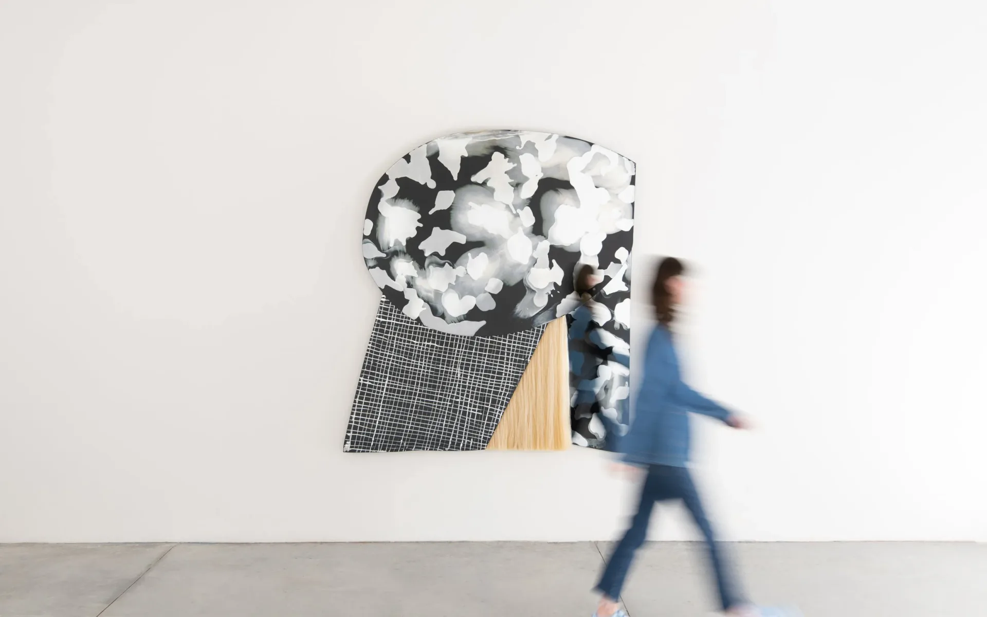 Abstract wall installation featuring layered geometric shapes in black, white, and natural wood tones with a blurred figure walking past by Ben & Aja Blanc.