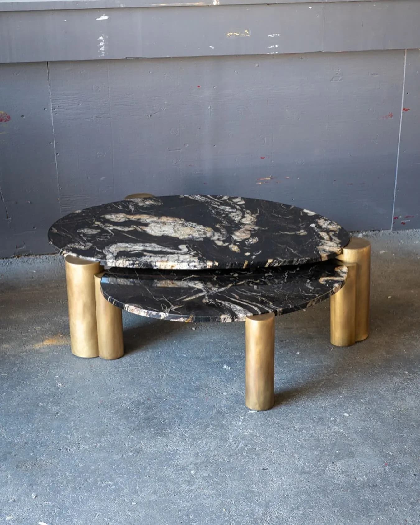 Black marble round coffee table with brass cylindrical legs on concrete floor against industrial wall by Ben Barber.