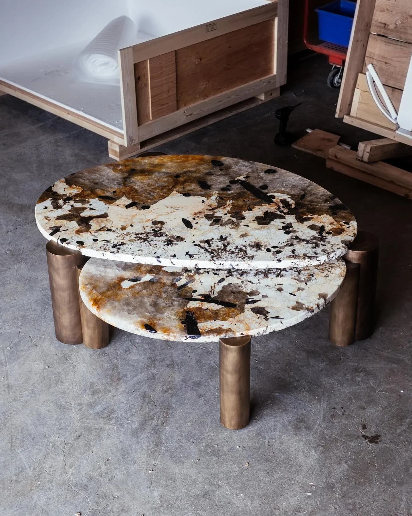 Organic-shaped white stone table with dark veining and wooden cylindrical legs in a workshop setting, by Ben Barber.