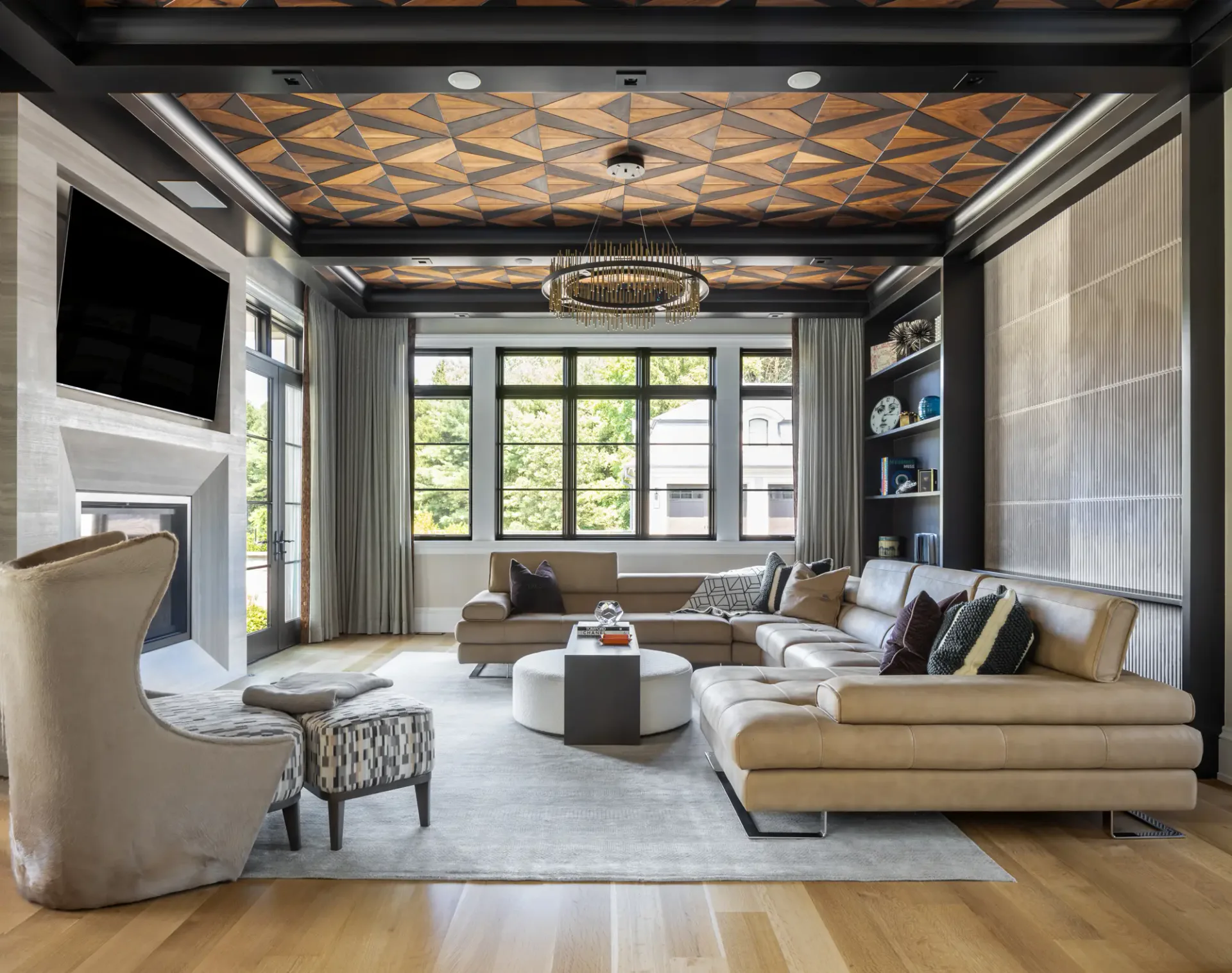Luxury living room with geometric patterned ceiling, large windows, curved tan sofa, and modern furnishings in warm neutrals by Beth Donner.