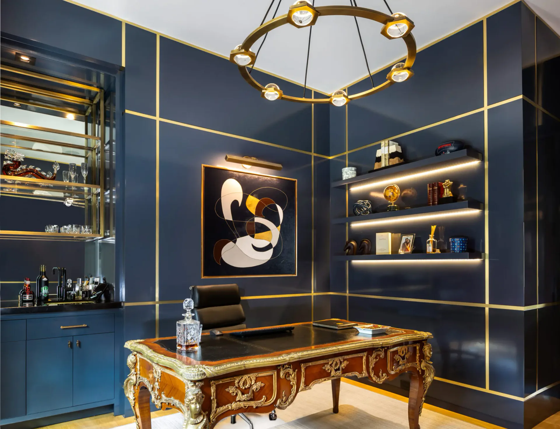 Luxurious navy office with gold trim, ornate desk, illuminated shelving, and geometric chandelier by Beth Donner.