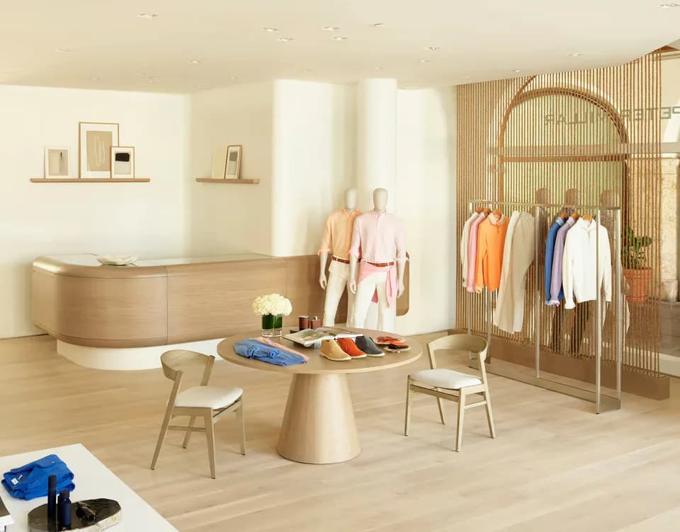 Warm minimalist retail clothing boutique with curved wooden counter, arched clothing racks, round pedestal table, and natural wood finishes by Betse Ungemack.
