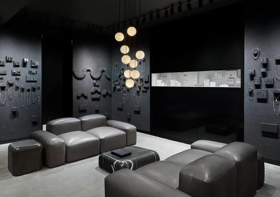 Modern lounge space with modular gray seating, suspended brass ball pendant lighting, and dark wall-mounted architectural elements by Betse Ungemack.