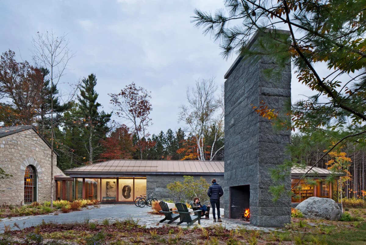 Modern chapel with stone tower and glazed walls set in woodland landscape with Adirondack chairs by Billie Tsien.