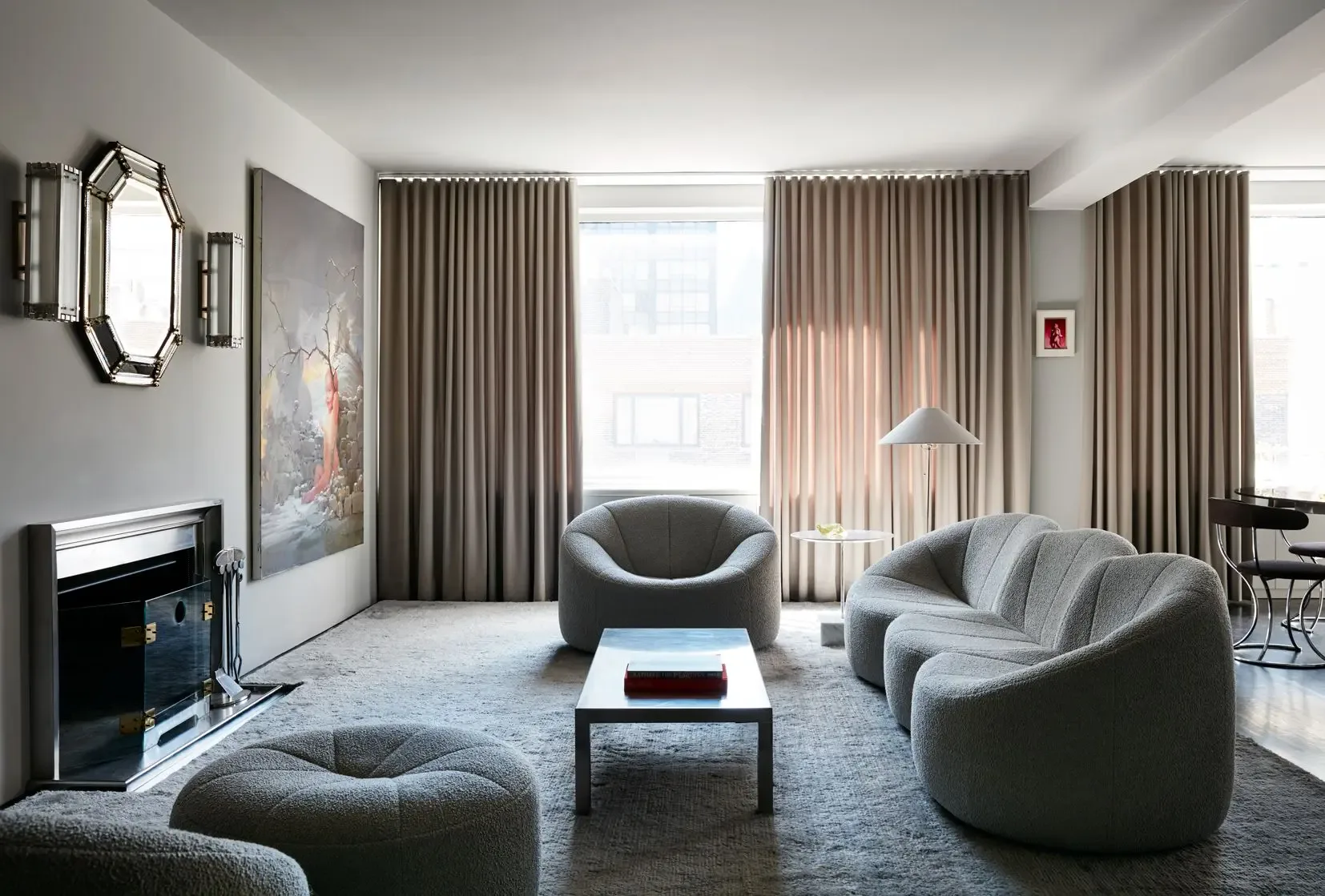 Modern living room with curved gray armchairs, taupe curtains, fireplace, and blue area rug designed by Billy Cotton.