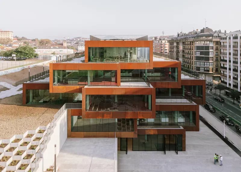 Aerial view of a striking orange-framed residential building with stacked, cascading volumes and extensive glazing, surrounded by urban context, by Bjarke Ingels.