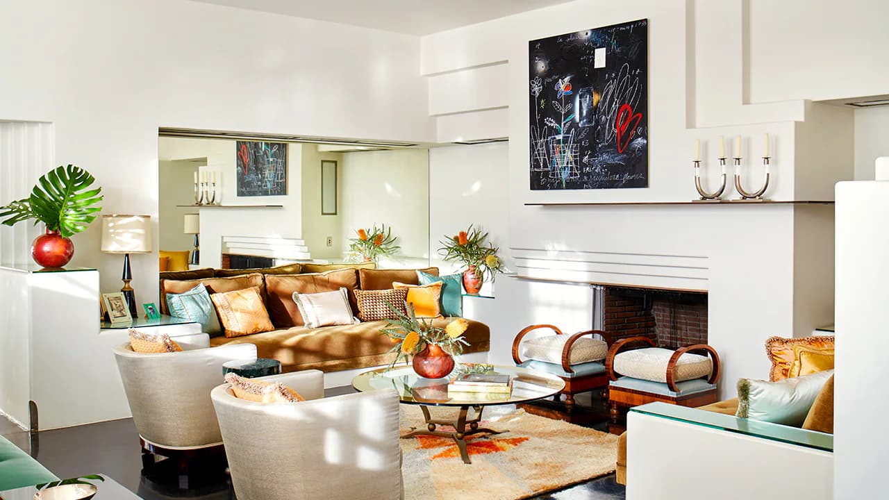 Luxe living room with gold velvet sofa, cream armchairs, fireplace, and curated art collection against soft neutral tones by Blue Williger.
