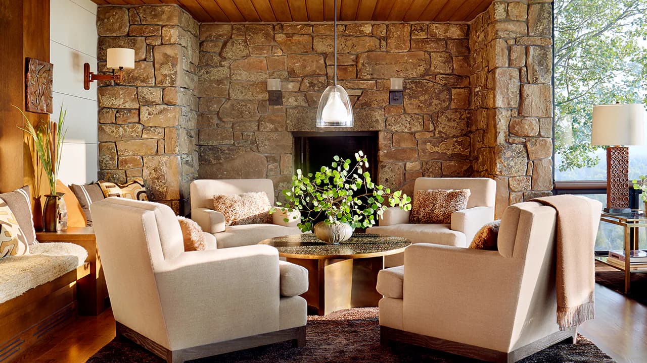 Luxurious living room with stacked stone walls, cream upholstered seating, wooden ceiling, and pendant lighting by Blue Williger.