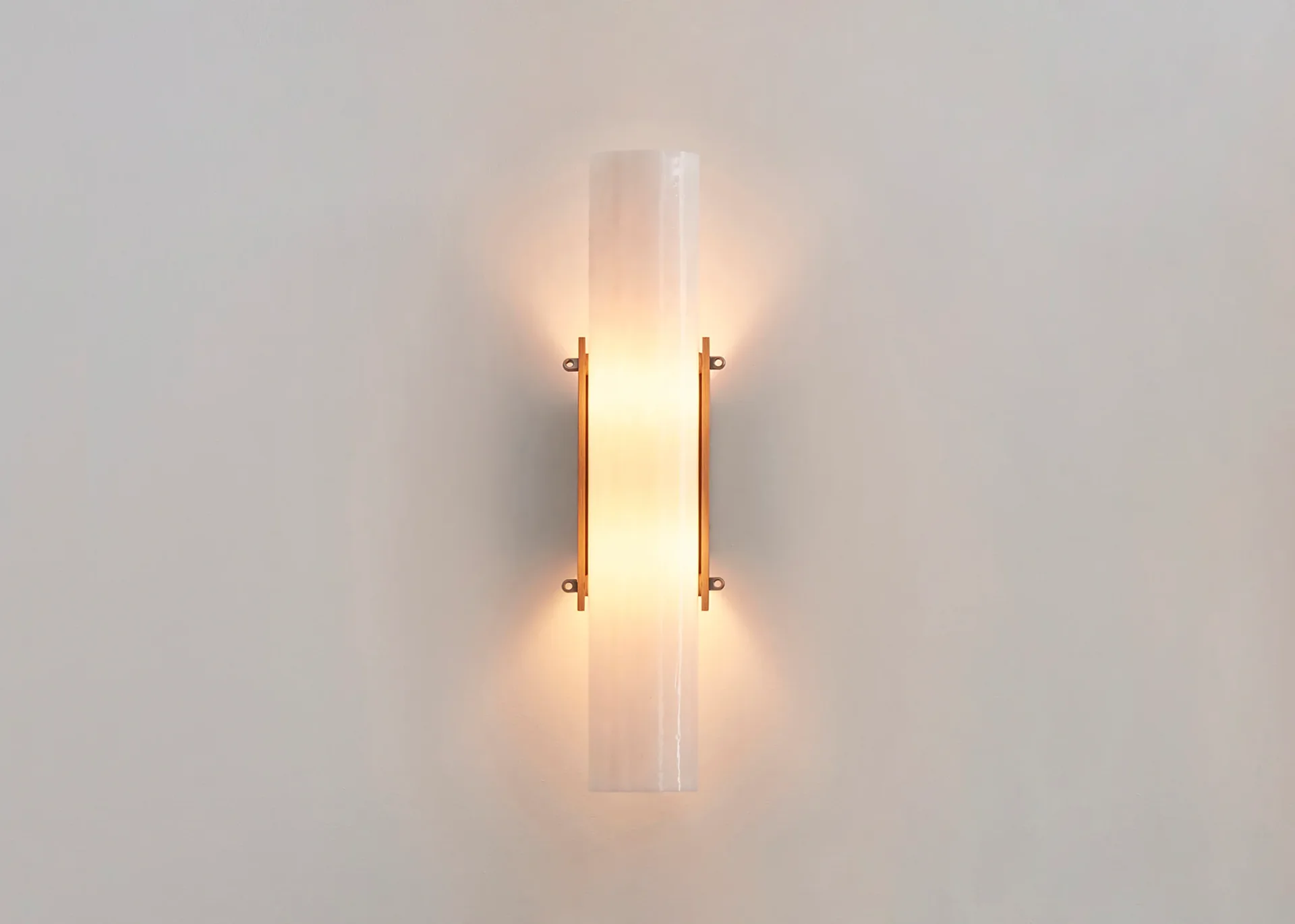 Minimalist wall sconce with cylindrical glass diffuser and brass fixtures emitting warm light, design by Bowen Liu.
