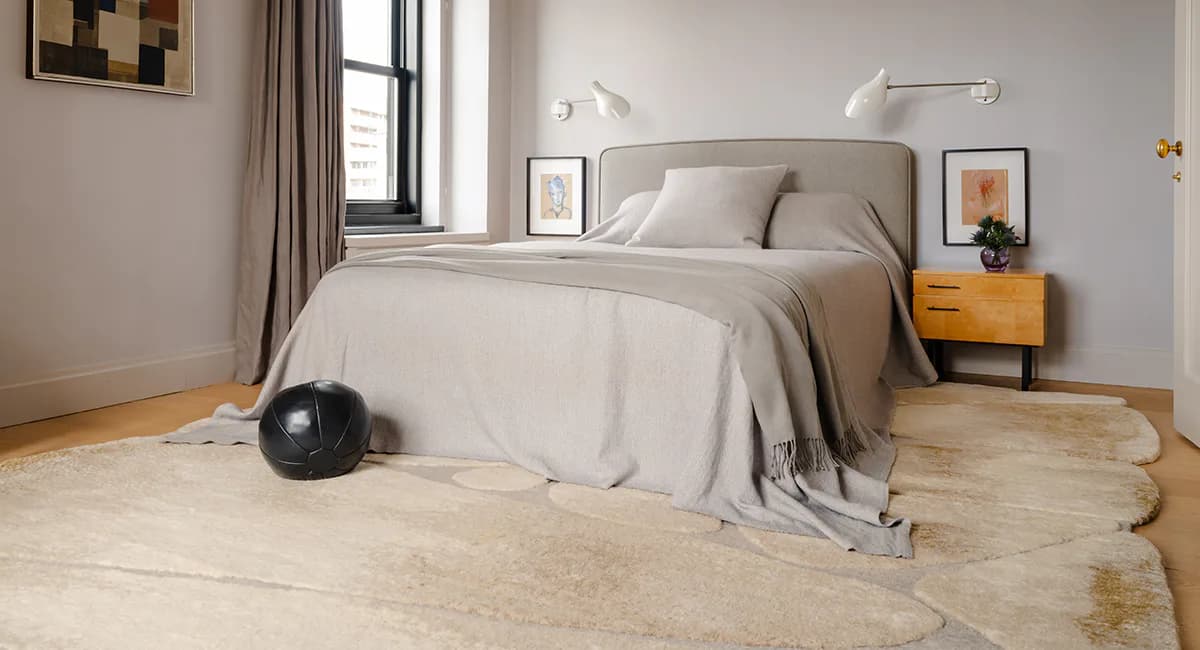 Modern bedroom with neutral palette features a curved headboard bed, yellow nightstand, and light wood flooring by Brad Davis.