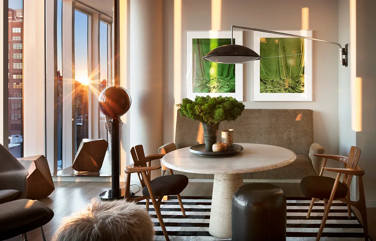 Modern dining room with round white pedestal table, mid-century wooden chairs, striped rug, and living plant installation on wall by Brad Ford.