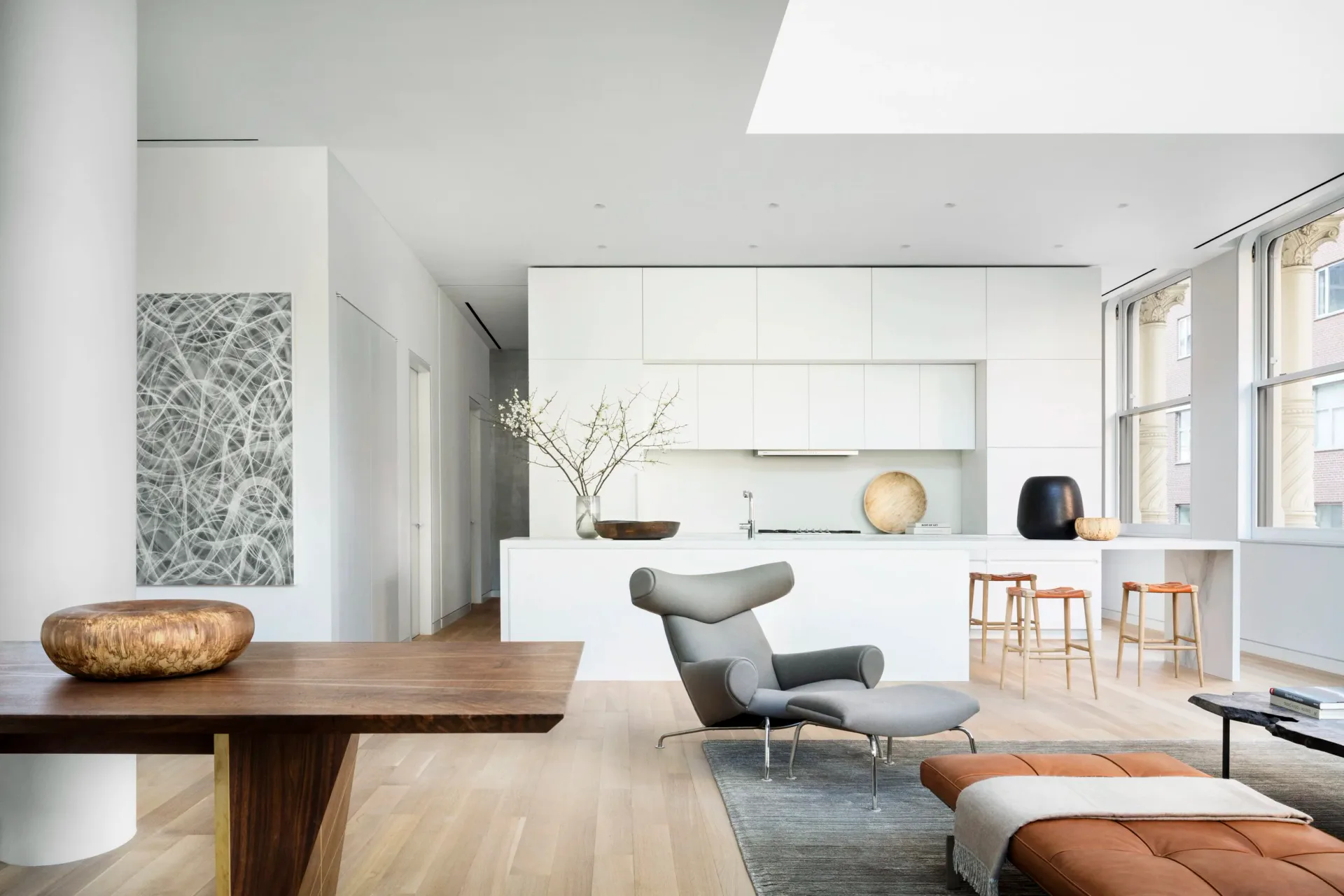 Modern living space with white cabinetry, wooden dining table, gray lounge chair, and skylight by Brad Ford.