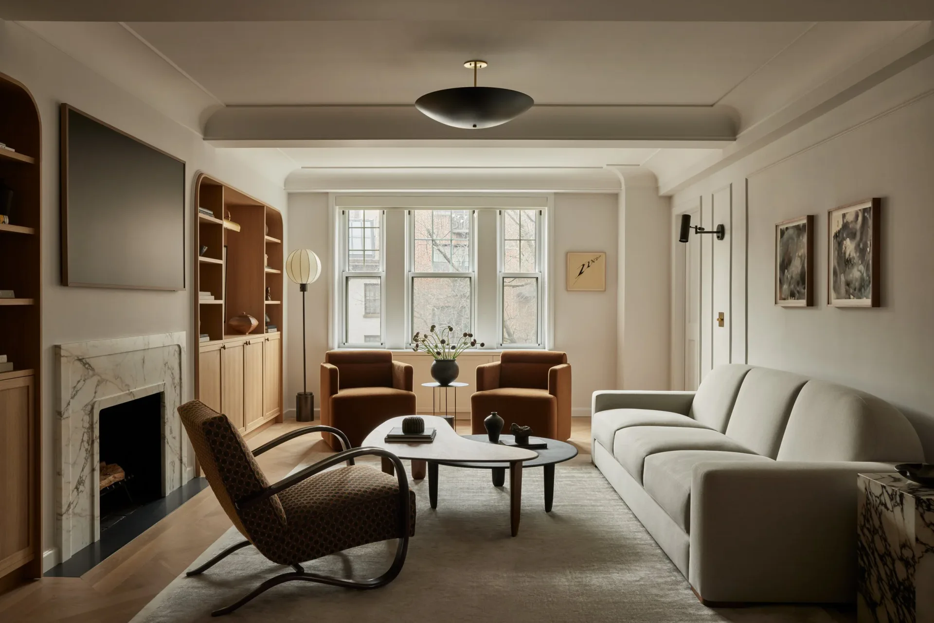 Modern living room with cream curved sofa, brown leather chairs, fireplace, and large windows, designed by Bradley Silling.