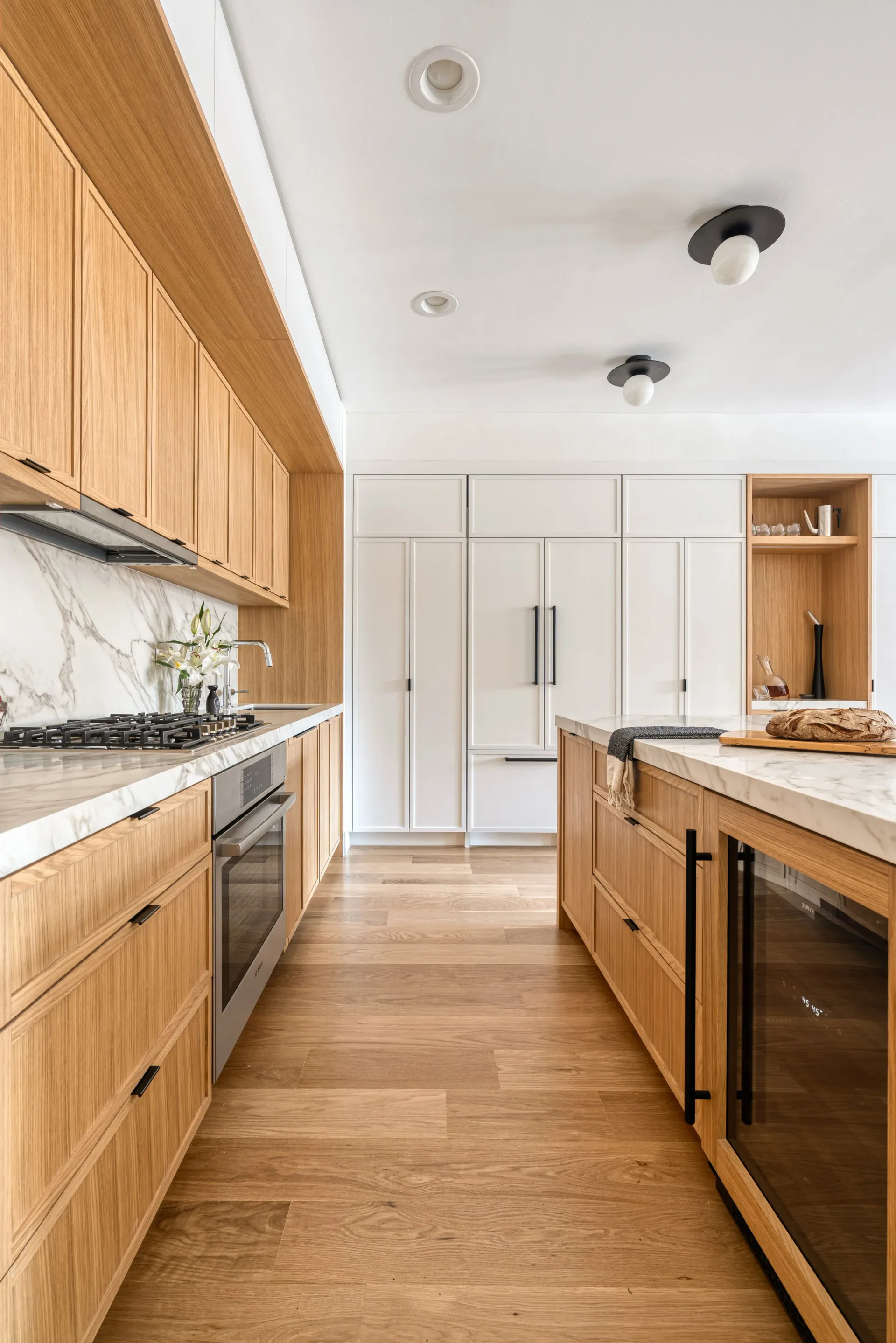 Modern kitchen with warm wood cabinetry, white subway tile backsplash, marble countertops, and stainless steel appliances, designed by Brenna Thompson.