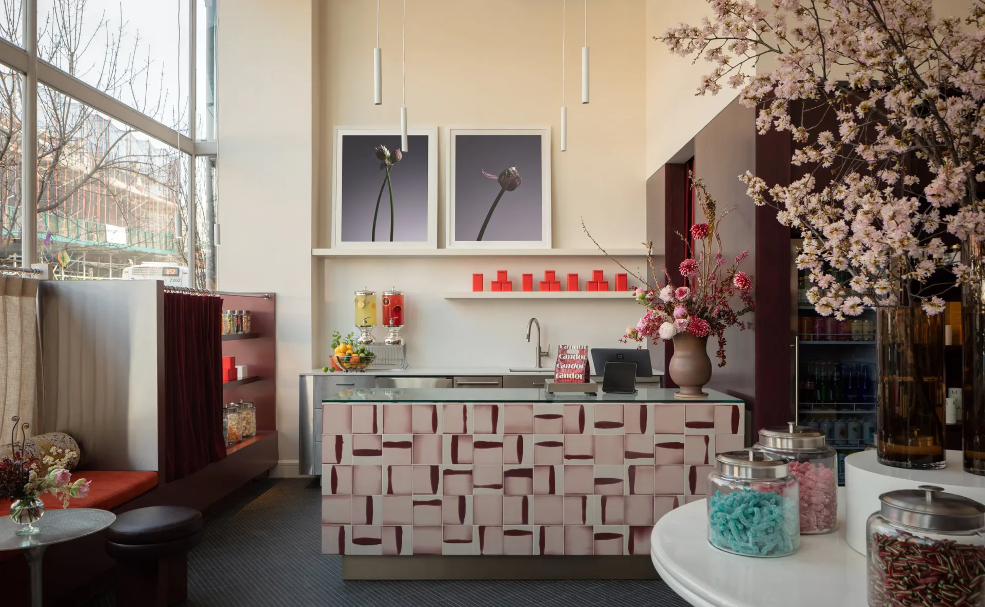 Modern hotel or spa reception area featuring a geometric patterned pink and white desk, cherry blossom arrangements, artwork, and warm neutral palette by Brian Cash.
