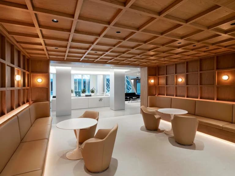 Warm wood-paneled lounge with coffered ceiling, cream seating pods, and minimalist furniture arrangement by Brian Orter.