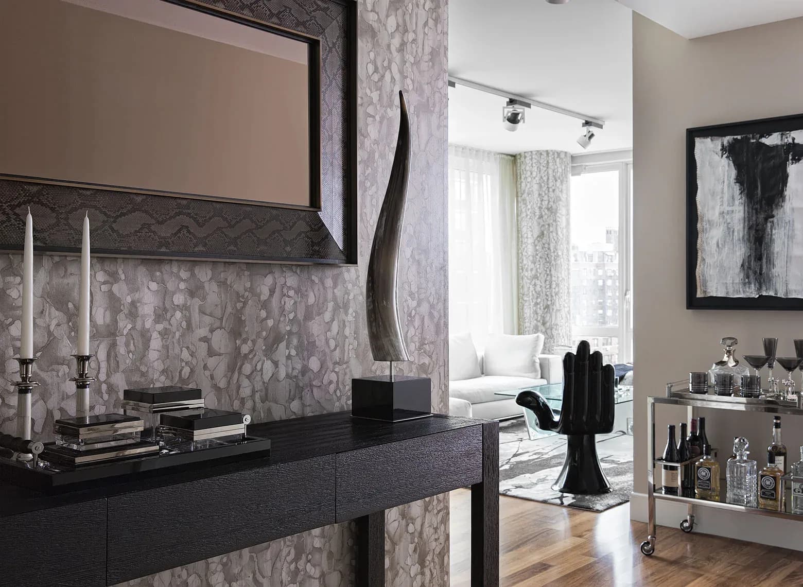 Modern bedroom with gray patterned wallpaper, black dresser, framed mirror, and elegant furnishings by Briana Kimball.